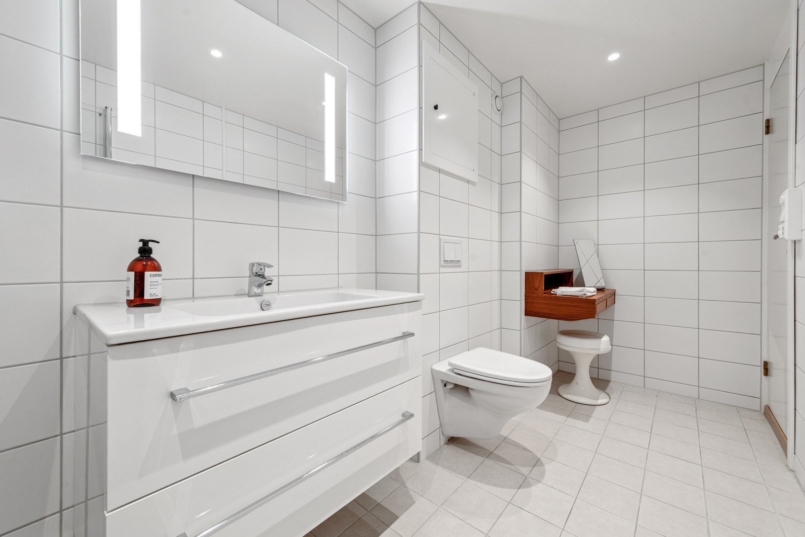 Badet er innredet med vegghengt toalett, servant med skuffer under og dusj i hjørne med innad slående dører. Galleribilde