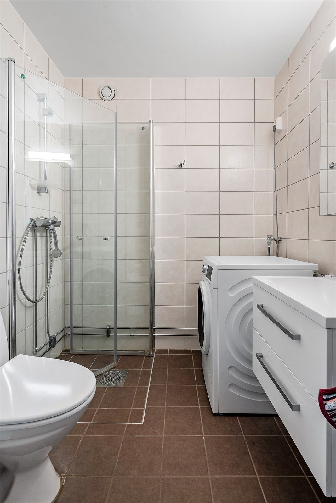 Dusjhjørne med glassdører, opplegg for vaskemaskin, toalett og vegghengt servant. Galleribilde