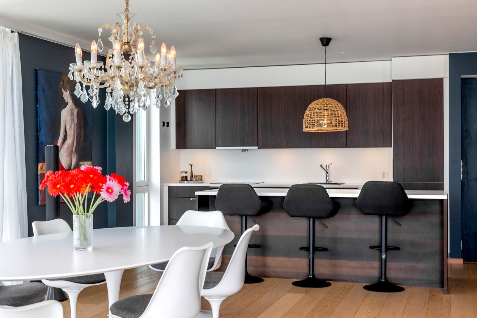 Kjøkkenet ligger tilbaketrukket i rommet og har en moderne innredning med mørke fronter og hvit Corian benkeplate Galleribilde