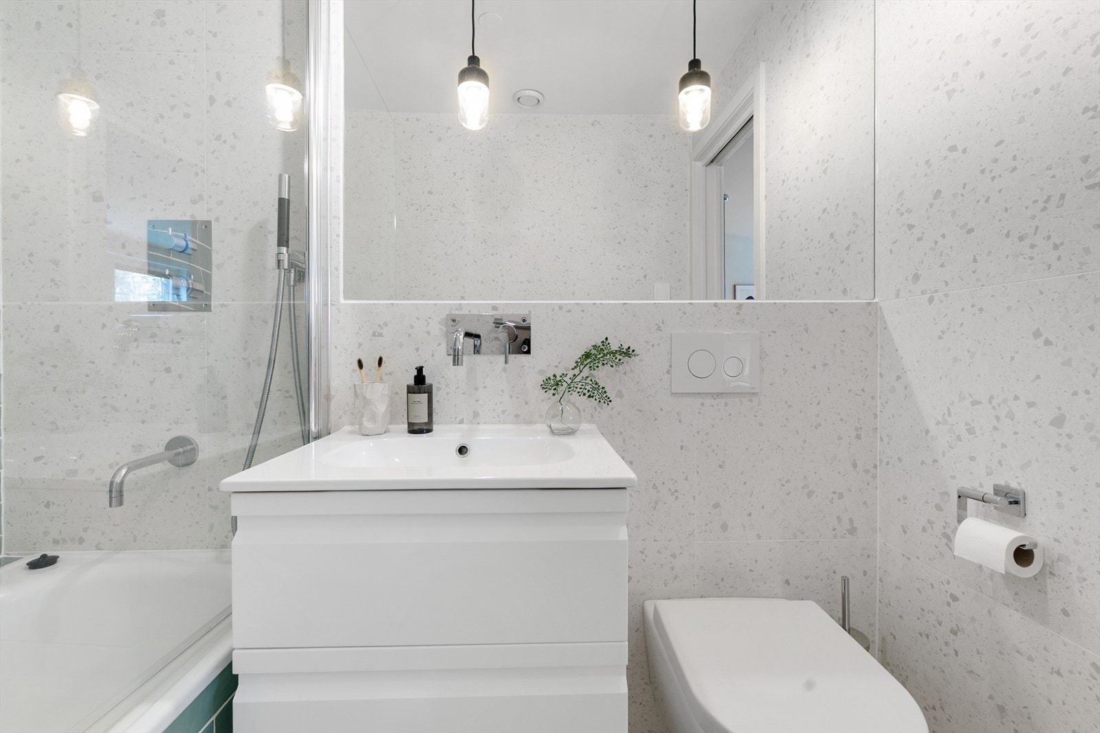 Badet har alt du trenger med pen baderomsinnredning med nedfelt vask og underskuffer, stort speil, vegghengt toalett og badekar med dusj. Galleribilde