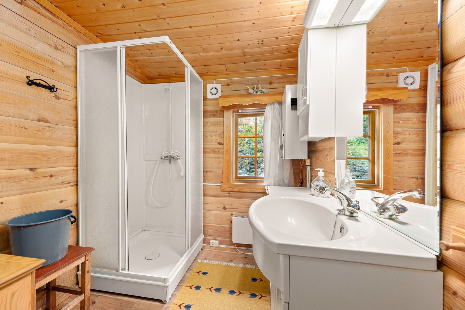 Enkelt hyttebad med innredning som inkluderer servant, dusjkabinett og liten gassdrevet vannvarmer. Galleribilde