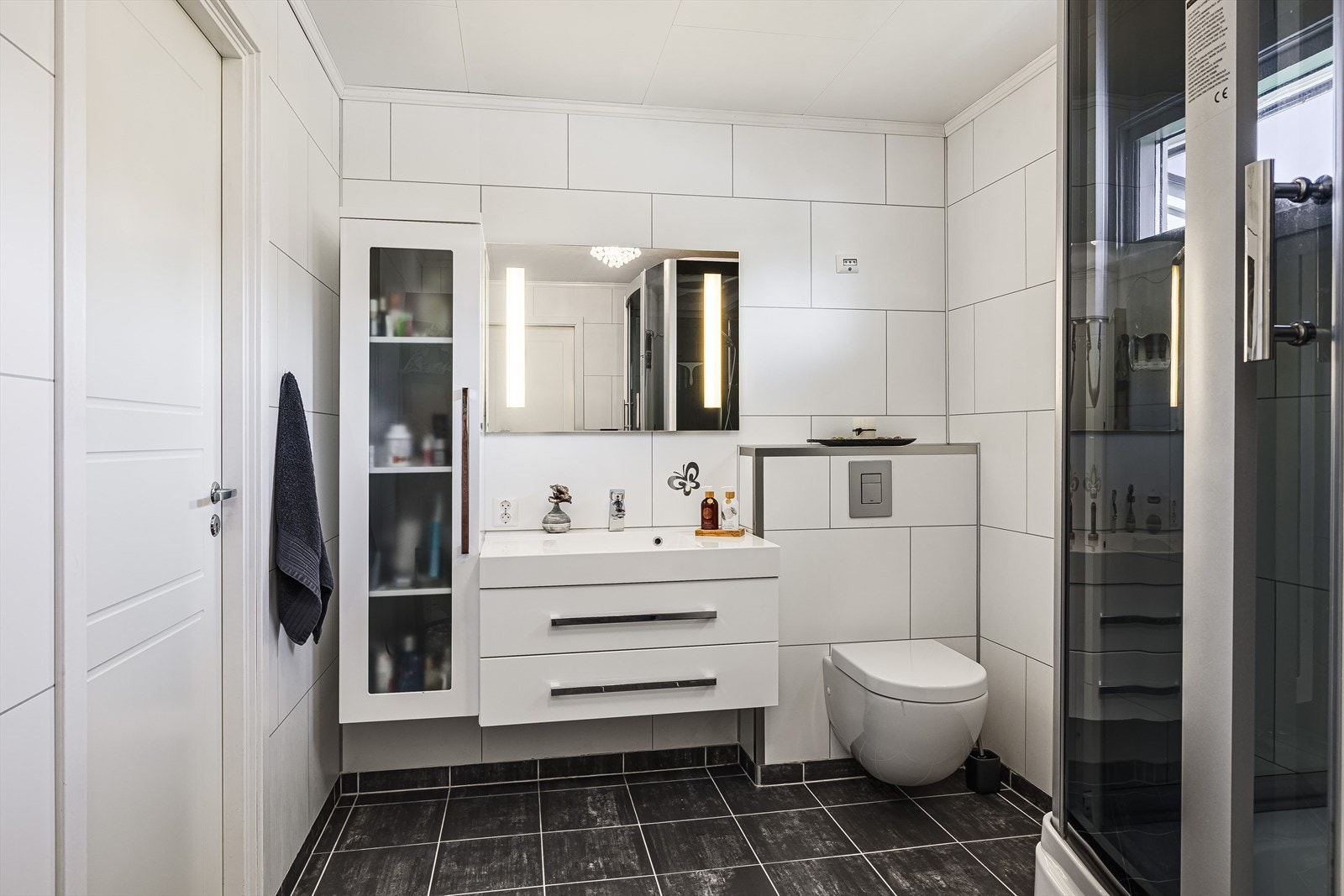 Pent, flislagt baderom med servant, baderomsinnredning, veggmontert toalett og dusjbad. Galleribilde