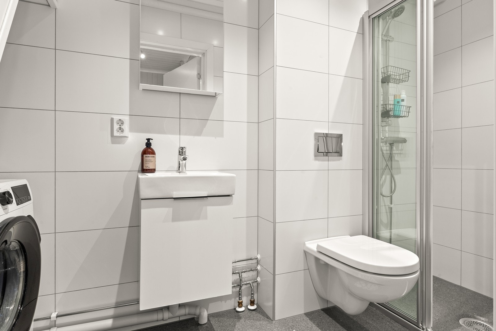 Badet er pusset opp i 2020 og har fliser på vegger og vinylbelegg på gulv. Rommet har innredning med servant, veggmontert toalett, dusjvegger/hjørne og opplegg for vaskemaskin Galleribilde