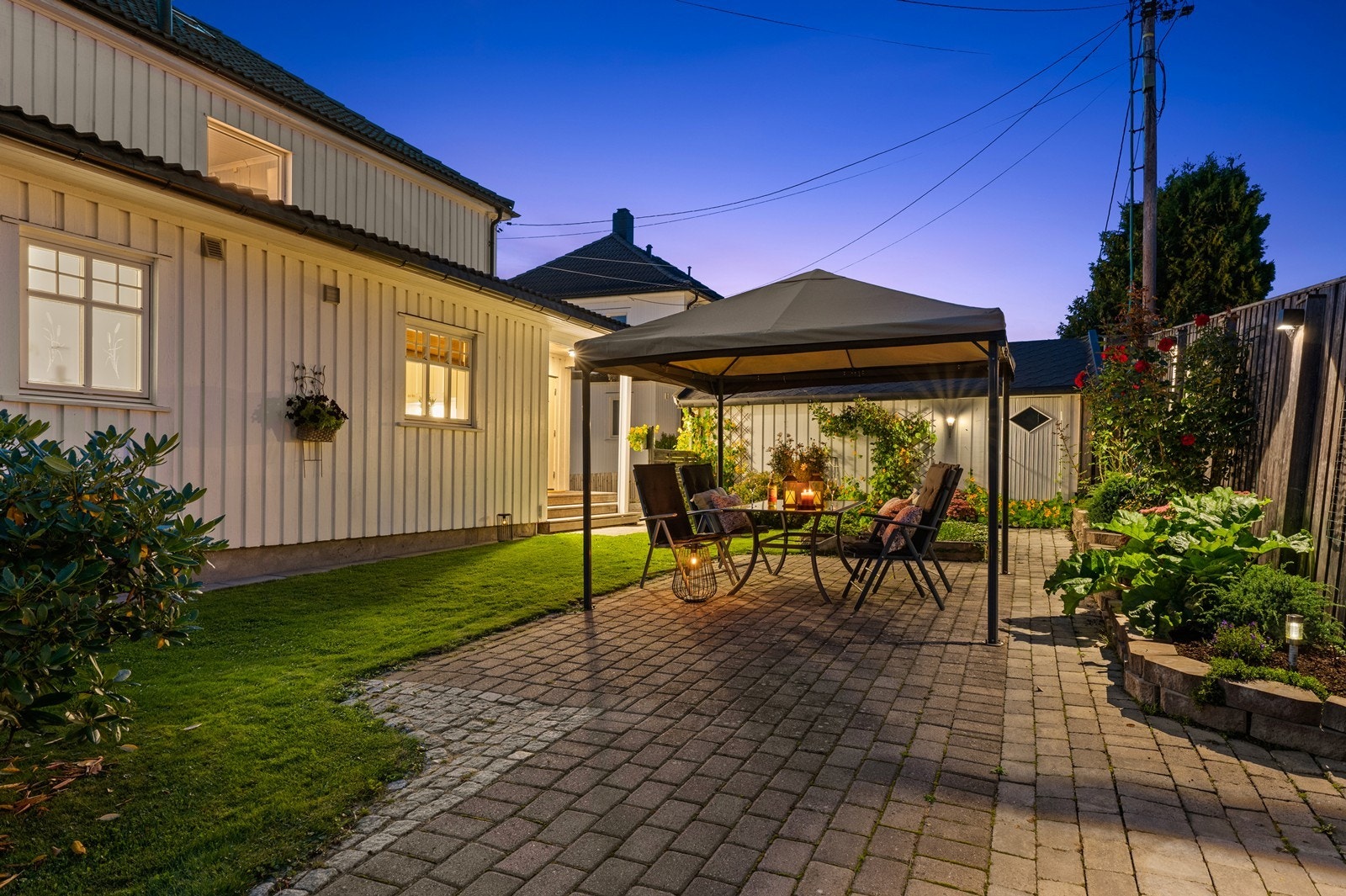 Hyggelig og skjermet bakhage som er pent opparbeidet med gressplen, stein og blomsterbed Galleribilde