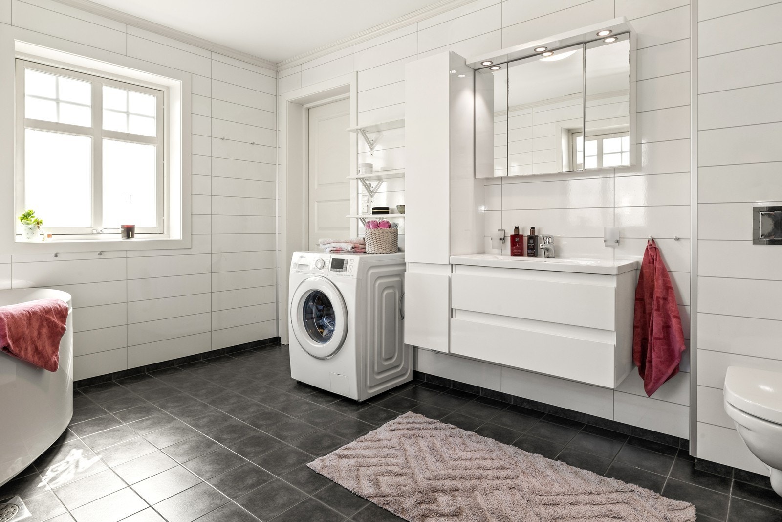 Badet er av god størrelse og har innredning med servant, veggmontert toalett, dusjkabinett, badekar og opplegg for vaskemaskin. Galleribilde