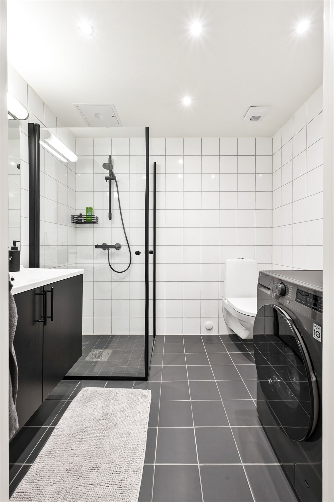 Stilrent bad med sorte detaljer på armatur og møblement. Det er opplegg til vaskemaskin på badet. Galleribilde