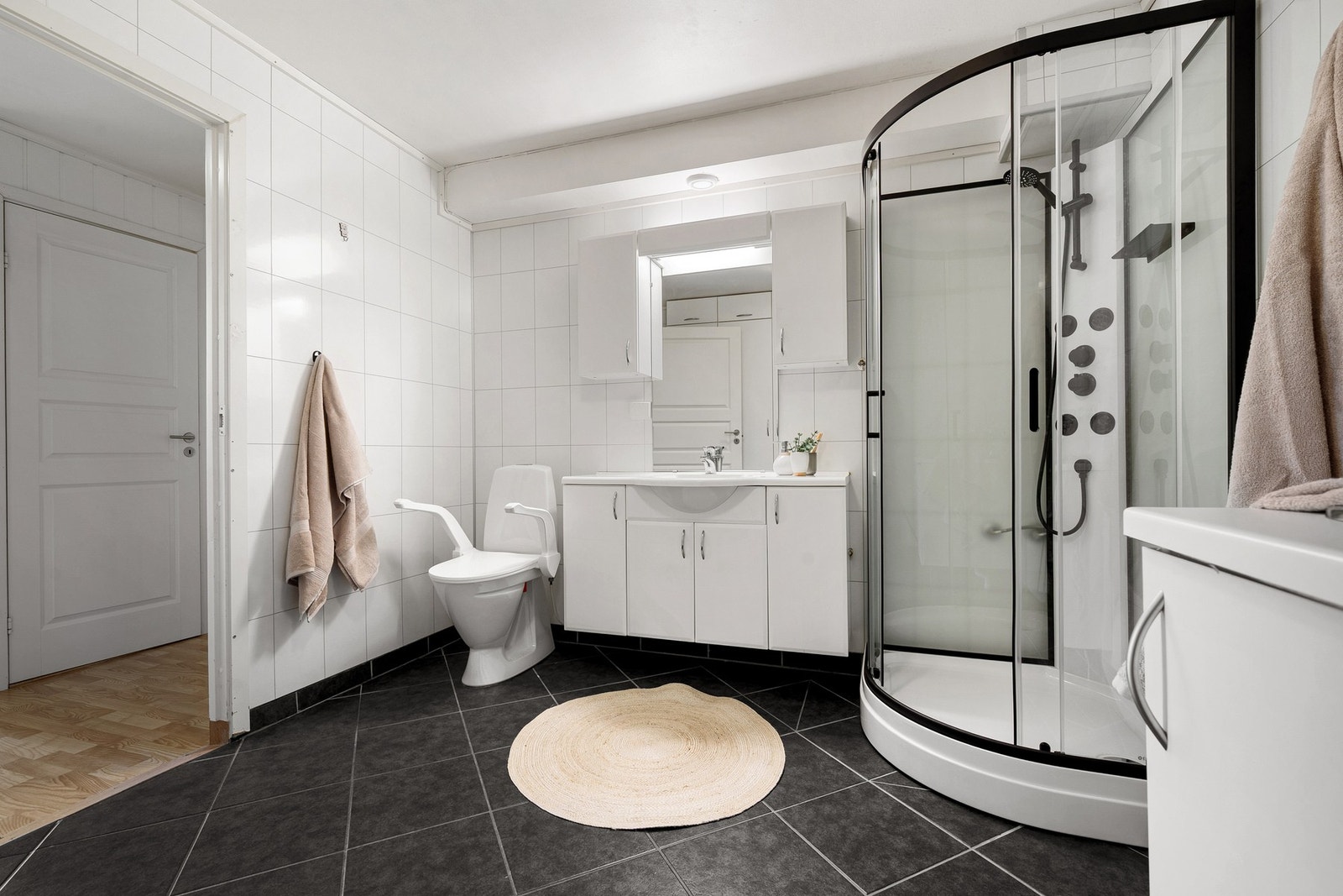 Badet har en praktisk innredning med helstøpt servant, overskap og speil Galleribilde