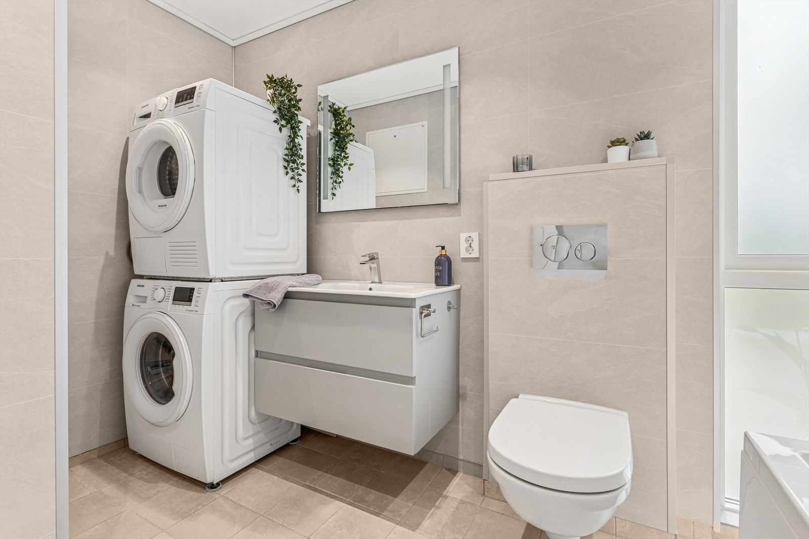 Badet er stilfullt innredet med vegghengt servant, speil med integrert belysning og vegghengt toalett. Det har også opplegg for vaskemaskin og tørketrommel. Galleribilde