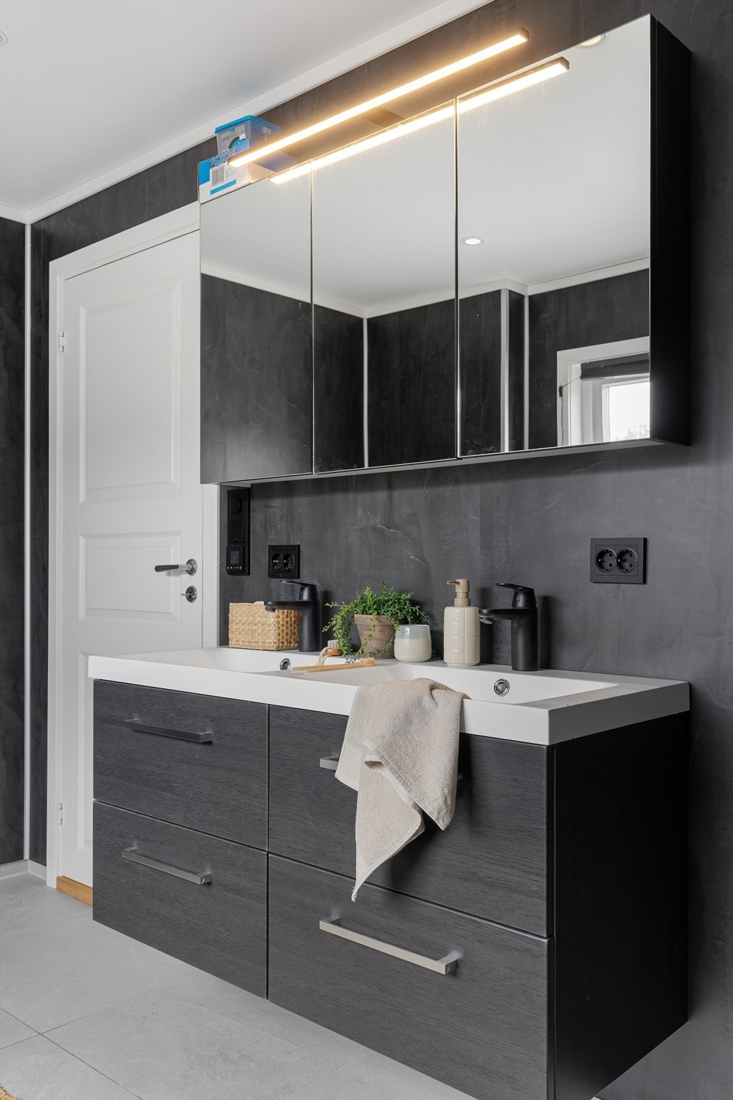 Romslig baderomsinnredning med underskap med skuffer og dobbel, heldekkende servant. I overkant av servanten er det speilskap med lyslist. Elektrisk uttak på vegg. Galleribilde