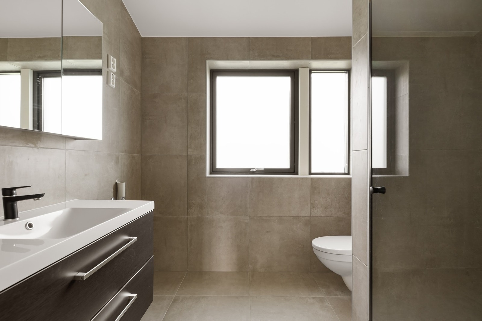 Flislagt bad med dusj, vegghengt toalett, nedfelt servant og skap. Galleribilde