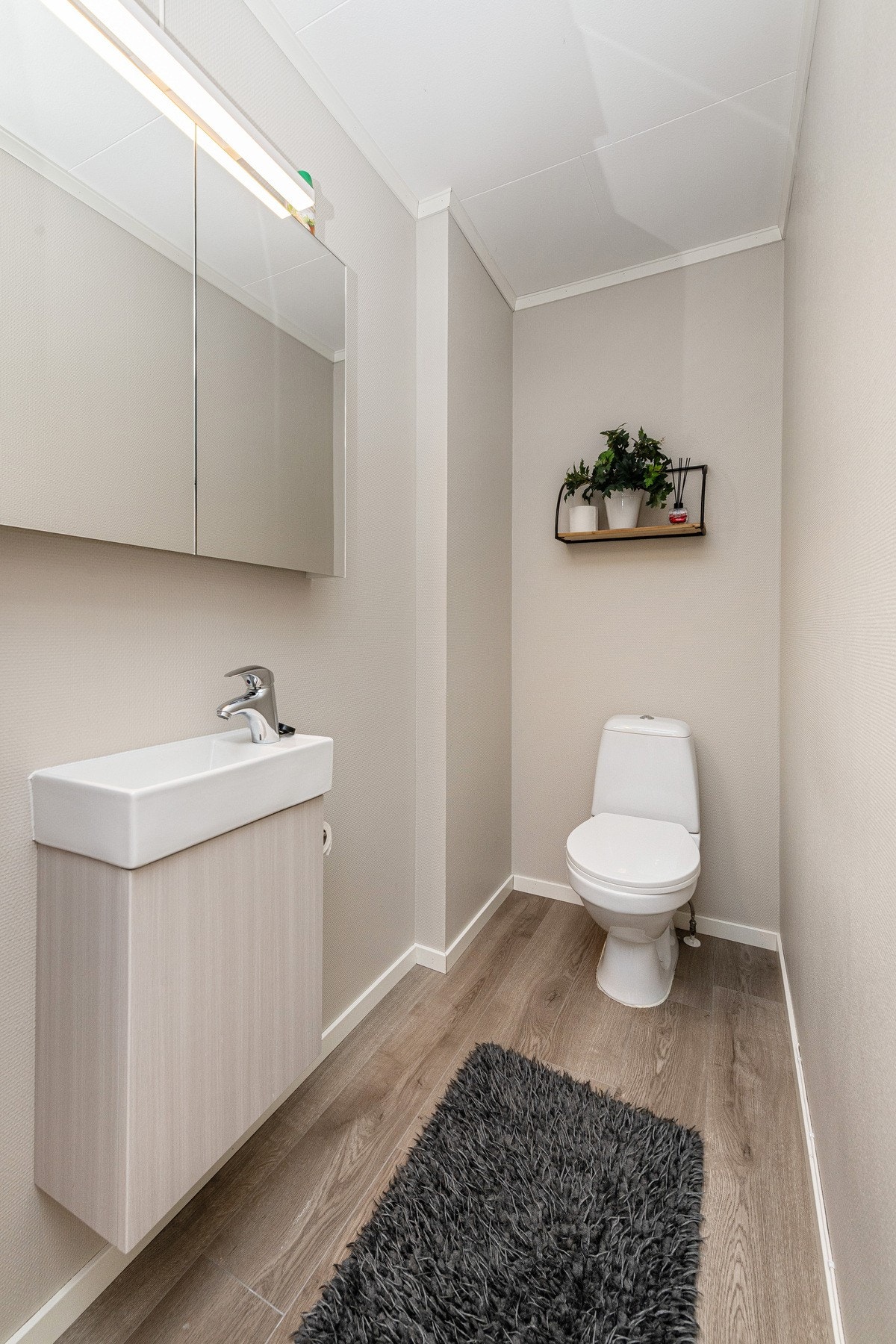 Separat toalettrom i første etasje med laminat på gulv, vegghengt servantskap og frittstående toalett. Praktisk plassert med enkel tilgjengelighet fra hovedetasjen. Galleribilde