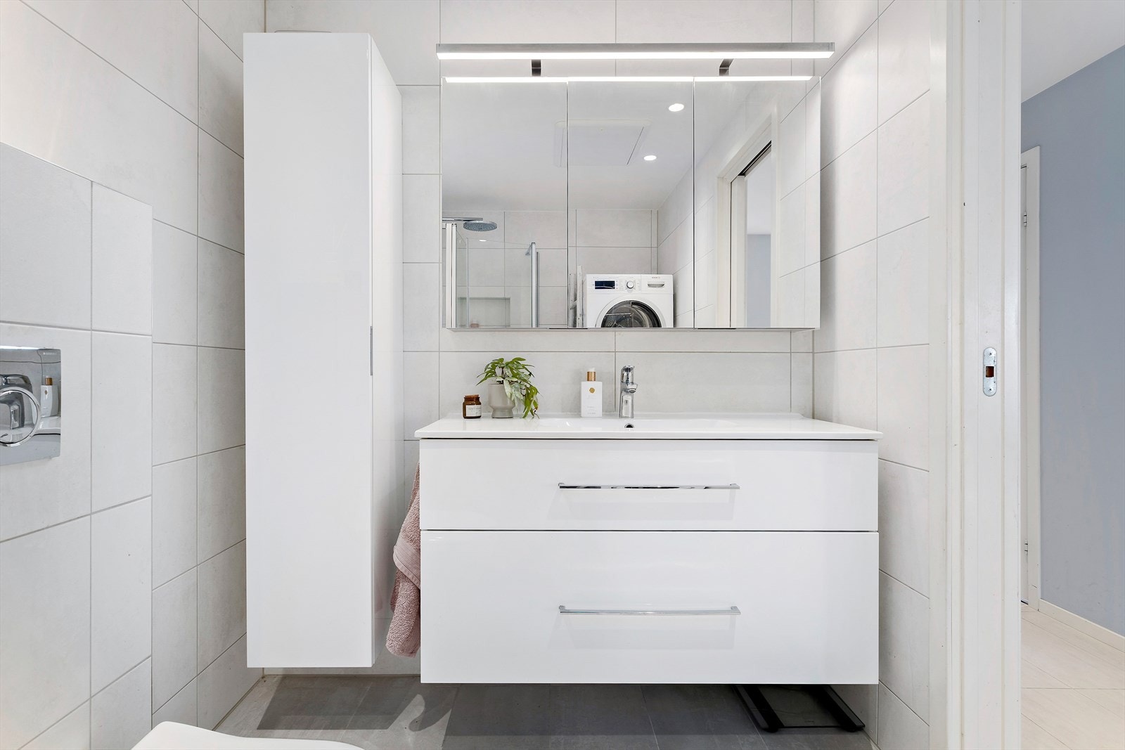 Innredningen fra Dansani består av et stilrent servantskap med glatte fronter, overlimt servant og ettgreps armatur fra HansGrohe. Over servanten er det speilskap med integrert belysning og tilhørende veggskap for ekstra oppbevaring. Galleribilde