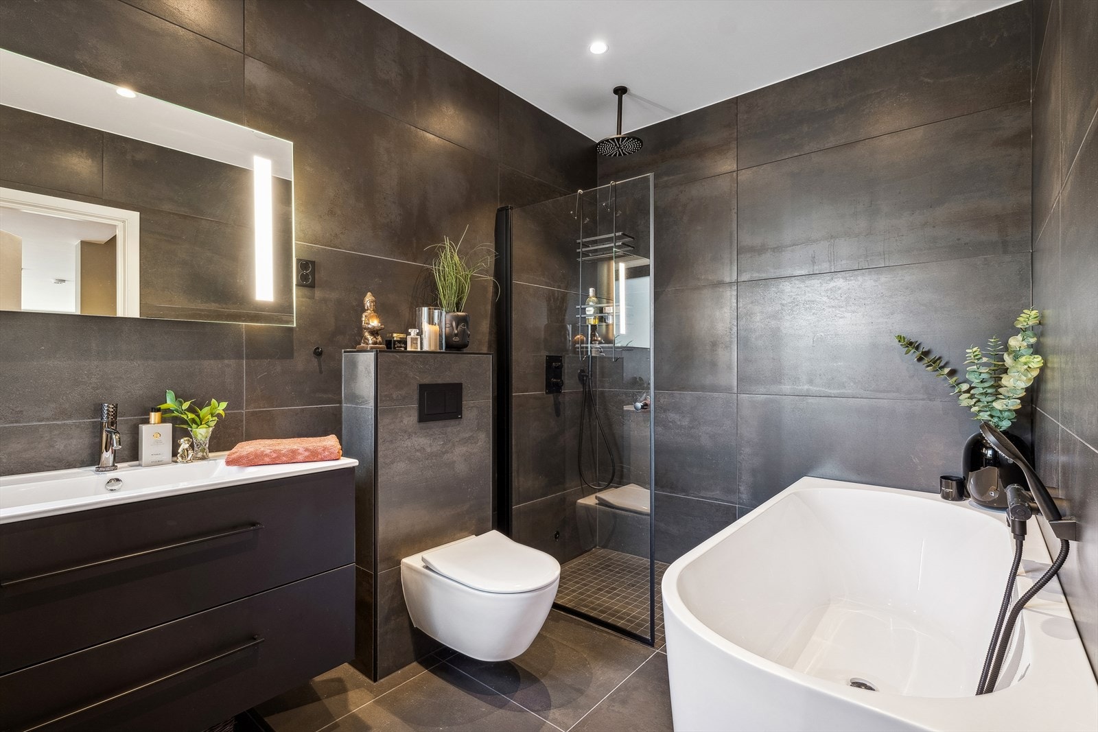 Delikat baderom med mørke fliser på vegg og gulv. Badet er utstyrt med varmekabel, badekar og egen rainshower. Galleribilde