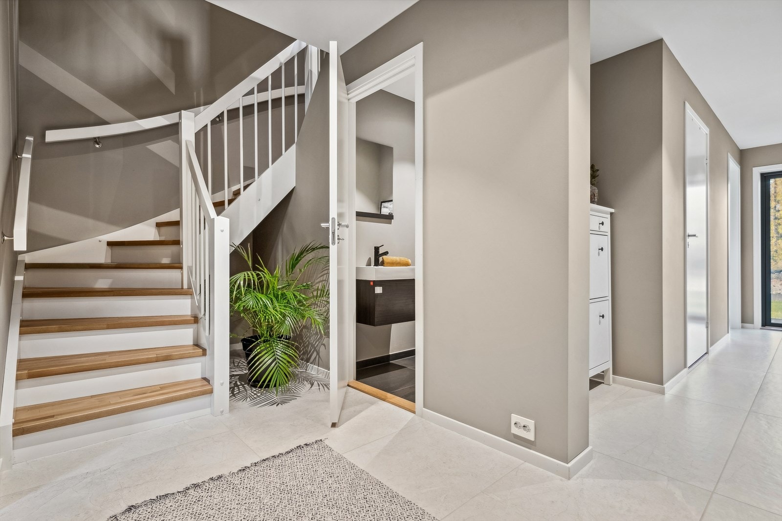 Romslig gang i 1.etg. med fliser og gulvvarme. Her har du tilgang til vaskerom, gang toalett, soverom, tekniskrom og egen utgang til markterrassen. Galleribilde