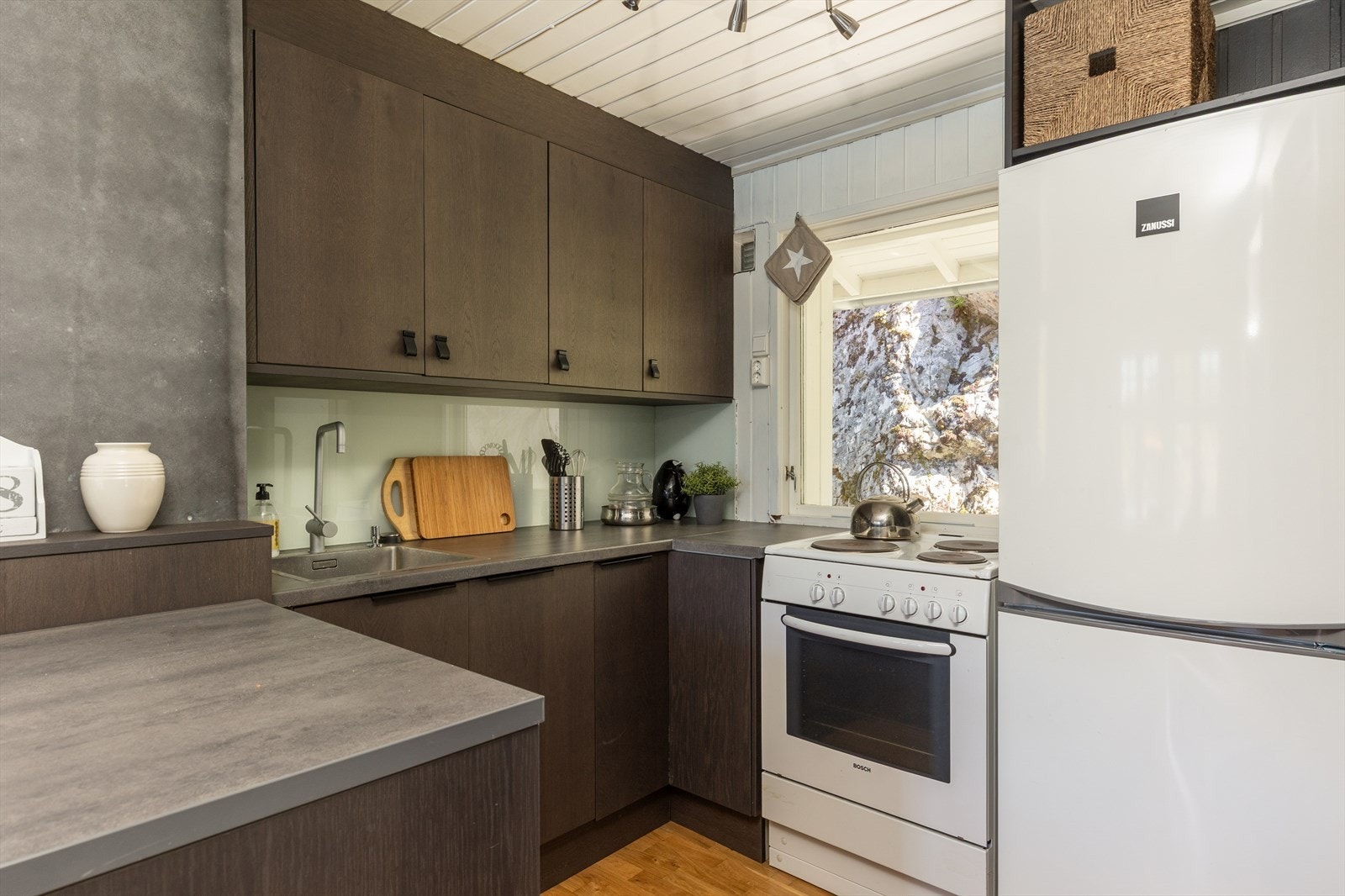 Innredningen er utført med slette fronter i mørk tre, benkeplate av høytrykkslaminat, og underlimt vask. Frittstående hvitevarer. Galleribilde