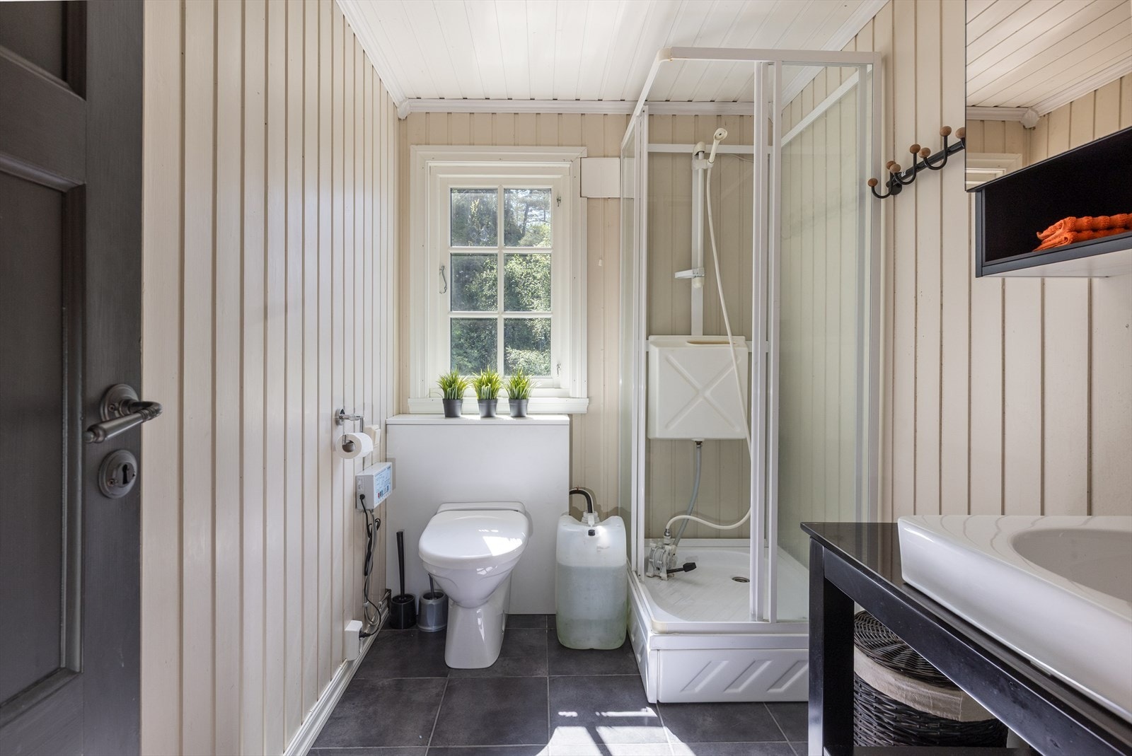 Badet har fliser på gulv, og panelplater på vegger. Badet er utstyrt med frittstående toalett, vask, og dusjkabinett. Galleribilde