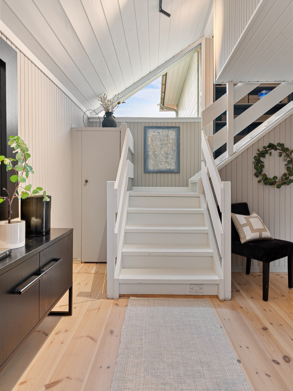 Lyst og åpent trappeløp med lagringskott til venstre og nedgang til kjeller til høyre. Galleribilde