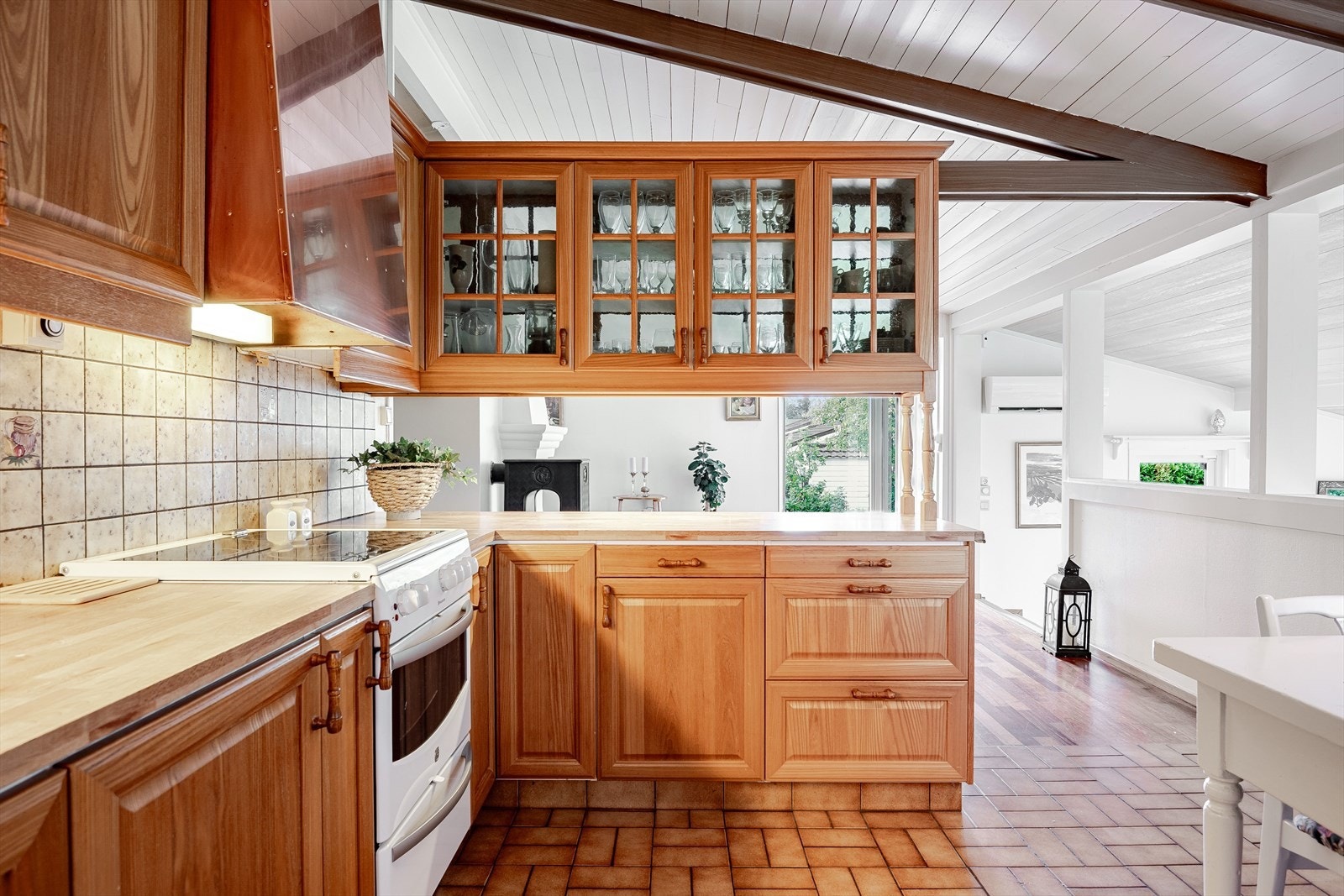 Kjøkkeninnredningen har en praktisk utforming som sørger for god skap- og benkeplass. Den åpne løsningen mot stuen er tilrettelagt for matservering, og overskapene har glassdører på begge sider. Galleribilde