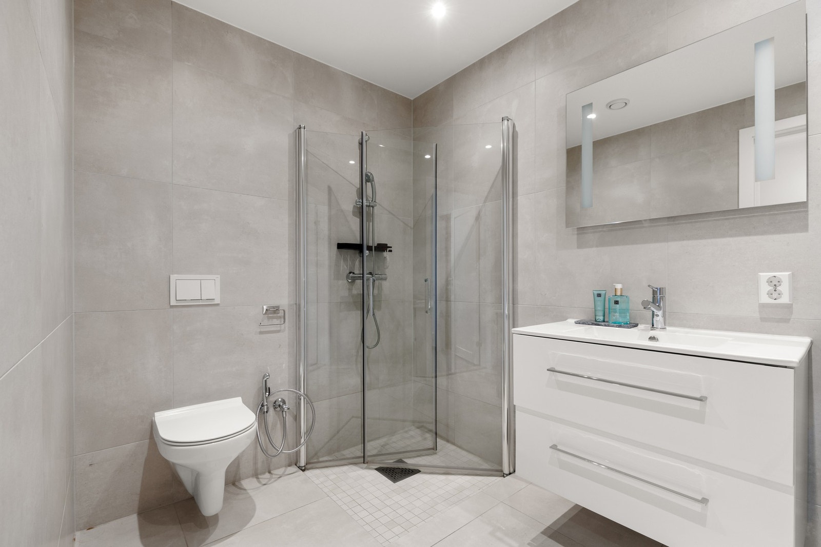 Moderne bad med dusjhjørne, vegghengt toalett og opplegg for vaskemaskin og tørketrommel. Galleribilde