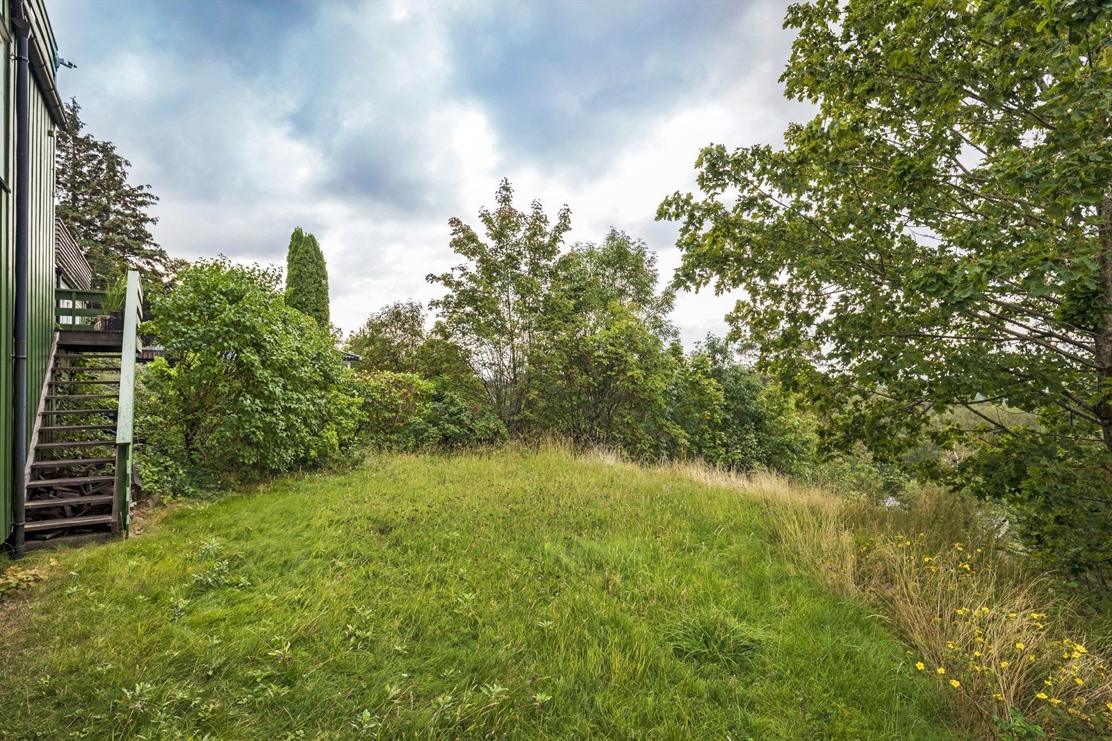 Tomten er skrånende, men her er delen flat og det er plass til for eksempel trampoline Galleribilde
