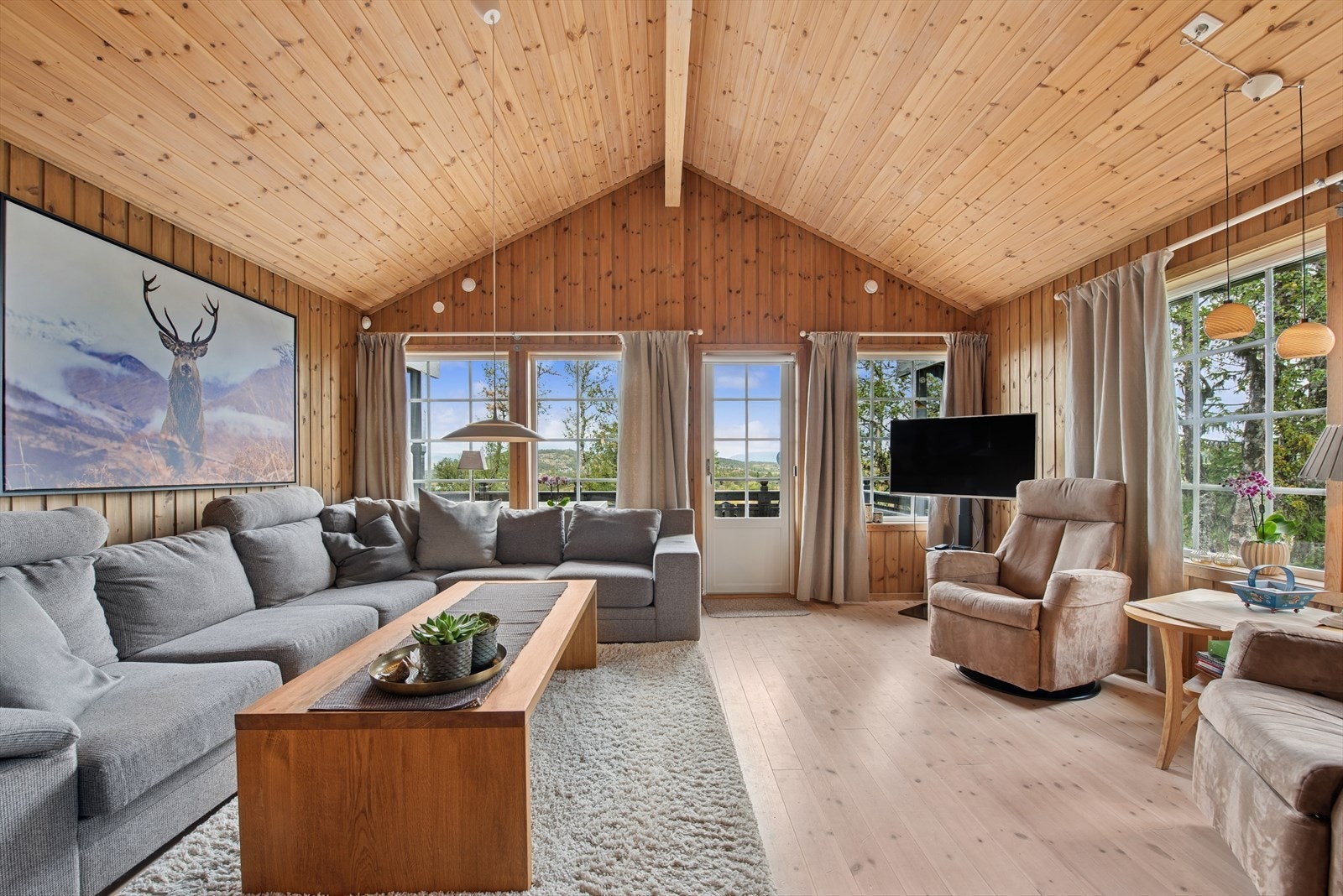 Lyse, store vindusflater mot nord og øst lar dagslyset strømme inn og binder stuen sømløst sammen med terrassen utenfor Galleribilde