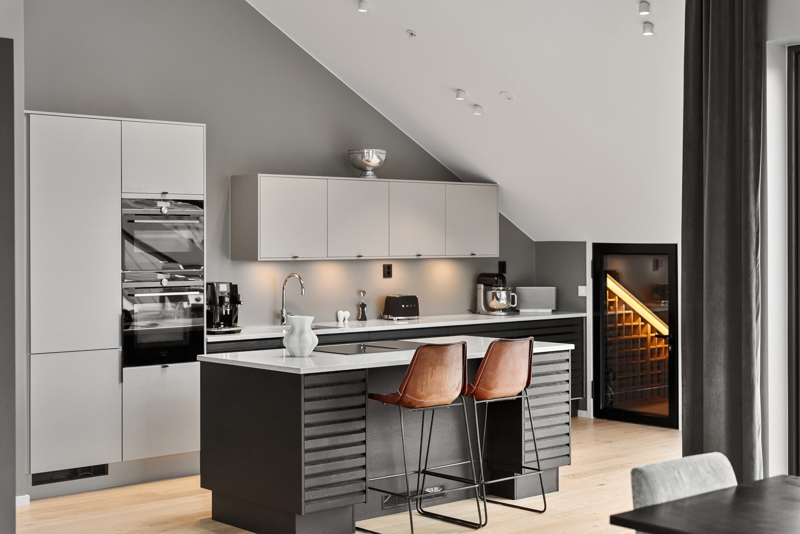 Med liggende trespiler på dører, glatte fronter på dører til høyskap/overskap og sidevegger på øya, gir dette kjøkkenet et moderne og elegant preg Galleribilde