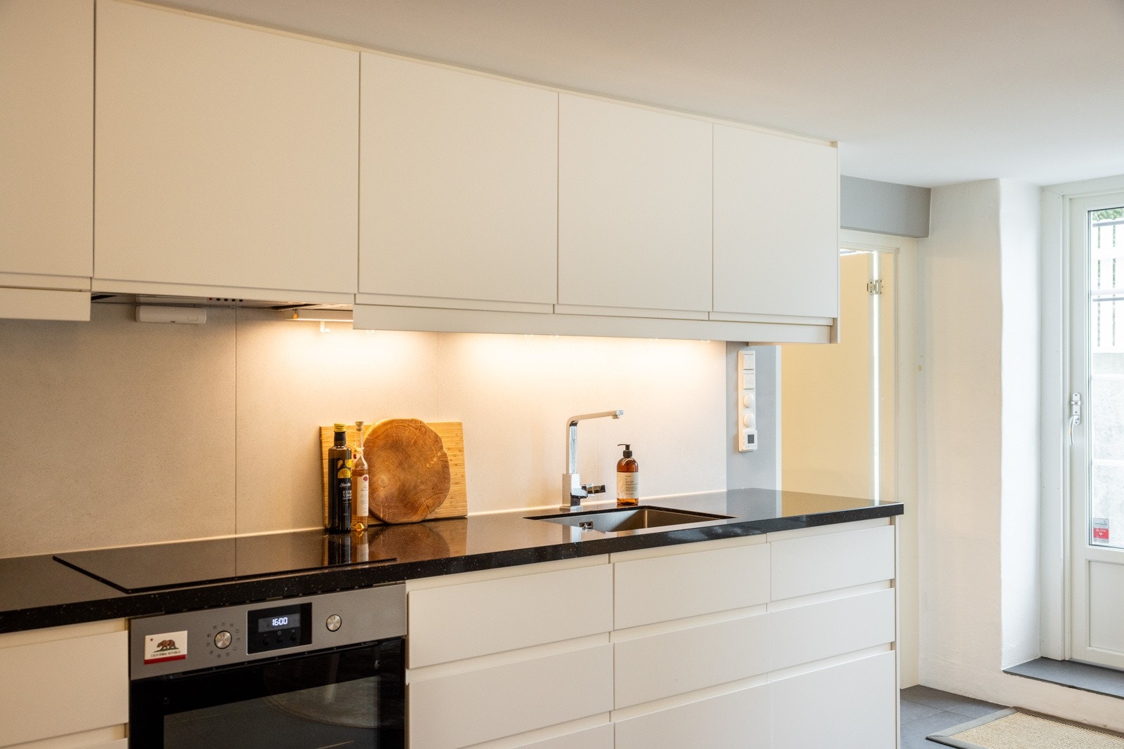 Stilren kjøkkeninnredning fra 2018 med integrert platetopp, stekeovn og oppvaskmaskin. Galleribilde