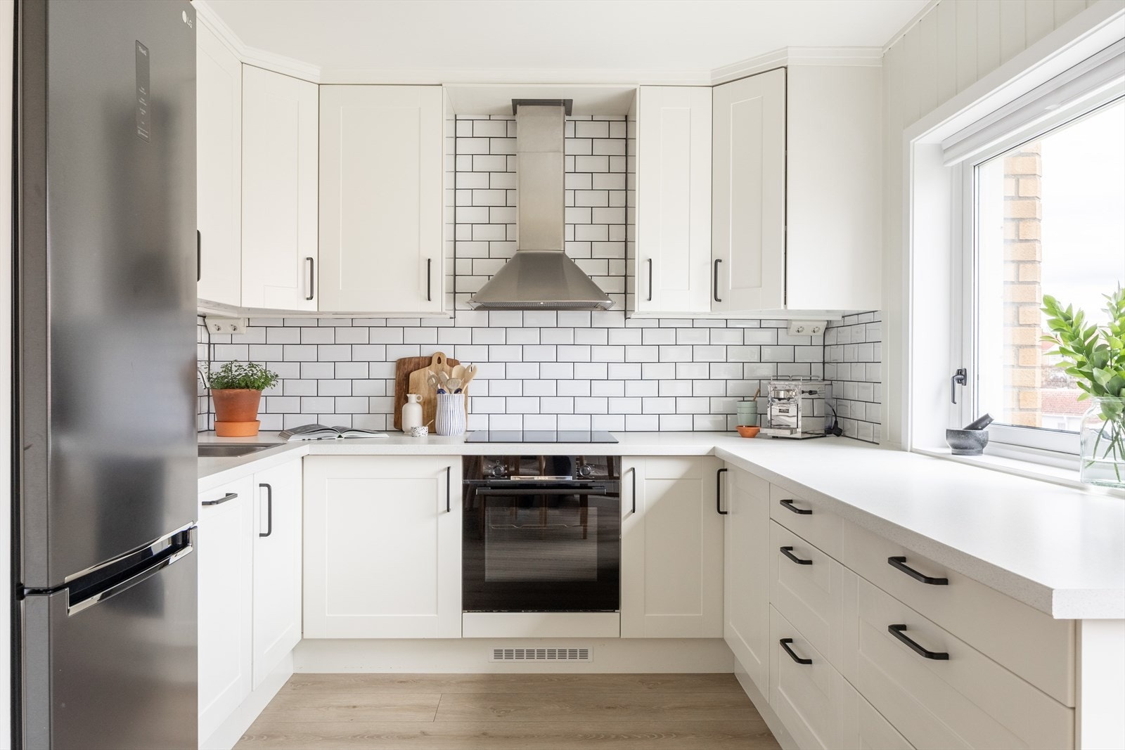 Lys og pen kjøkkeninnredning med profilerte fronter, belysning under overskap og fliser på vegg over benkeskap Galleribilde