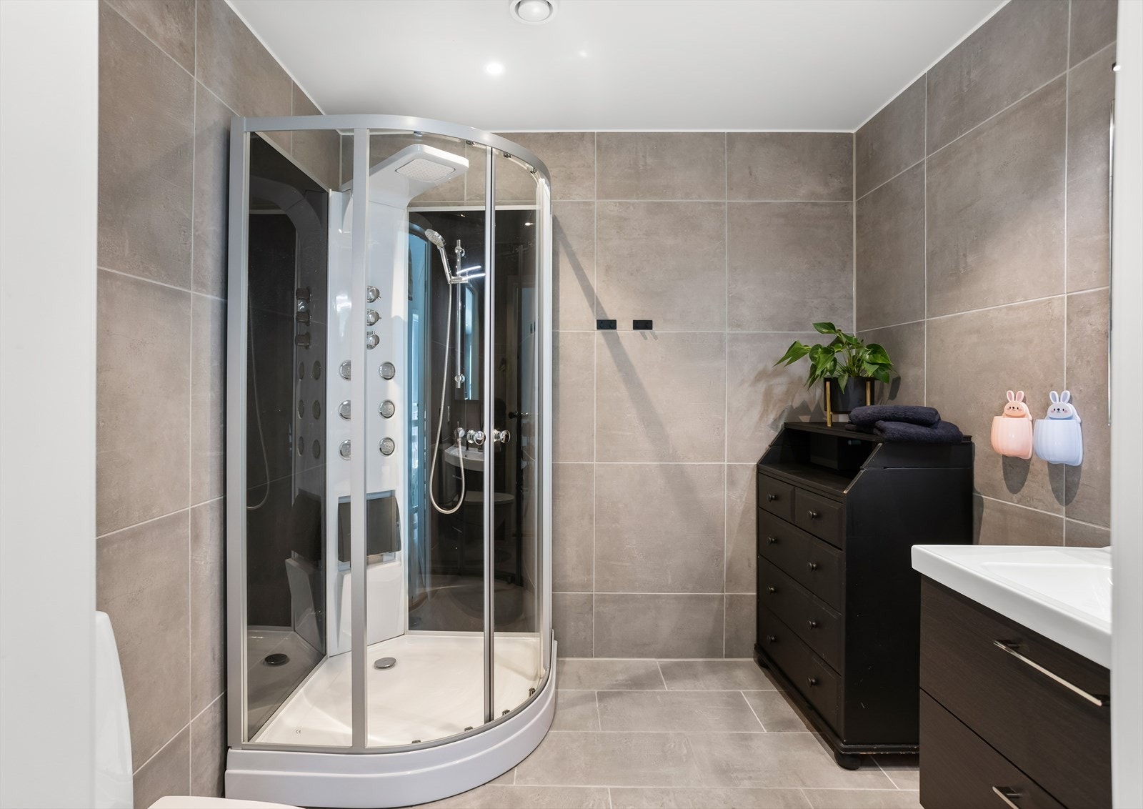 Rommet er innredet med servantskap med mørke/glatte fronter, speil med lys, toalett og dusjkabinett. Galleribilde