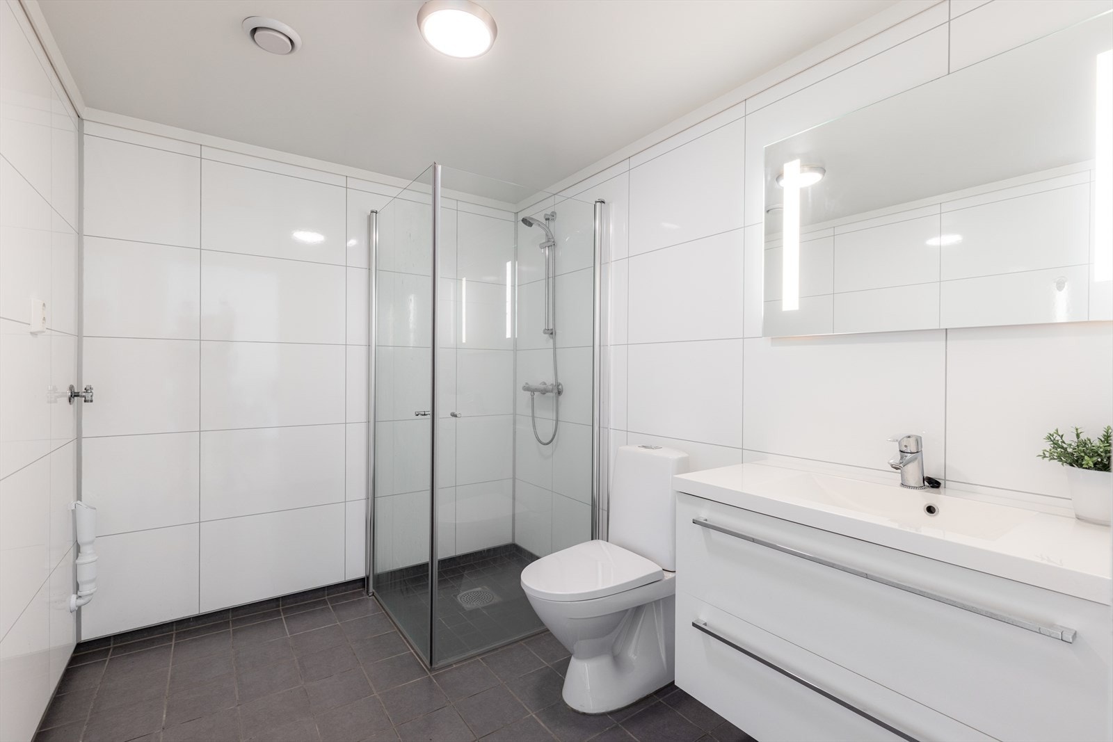 Badet inneholder dusjhjørne med vegger, toalett og servant med underskuffer, speil og lys. Det er opplegg for vaskemaskin og tørketrommel. dusjvegger/hjørne. Det er balansert ventilasjon. Galleribilde