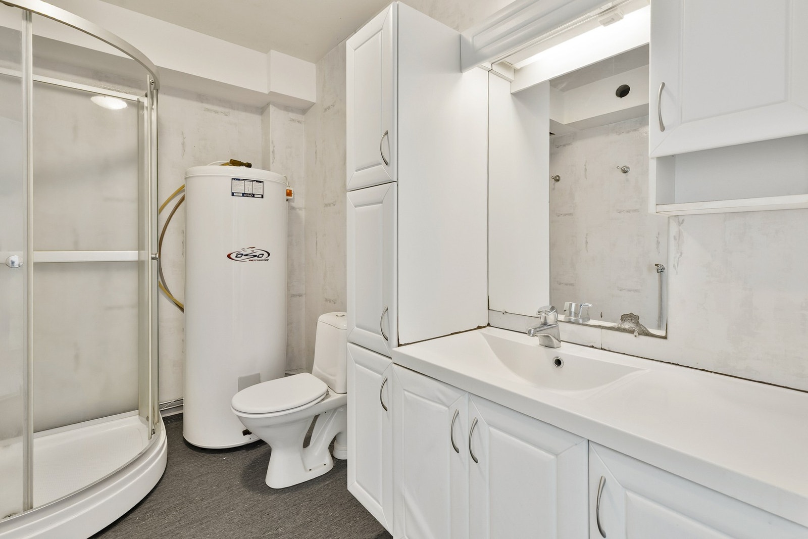 Baderom med dusjkabinett, toalett, servant, baderomsinnredning og varmtvannsbereder. Galleribilde