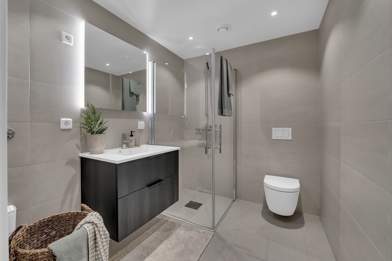 Delikat helfliset baderom med gulvvarme. Badet er utstyrt med sandfargede fliser, downlights i taket og stilfull innredning fra HTH. På badet er det god plass til vaskemaskin og tørketrommel Galleribilde