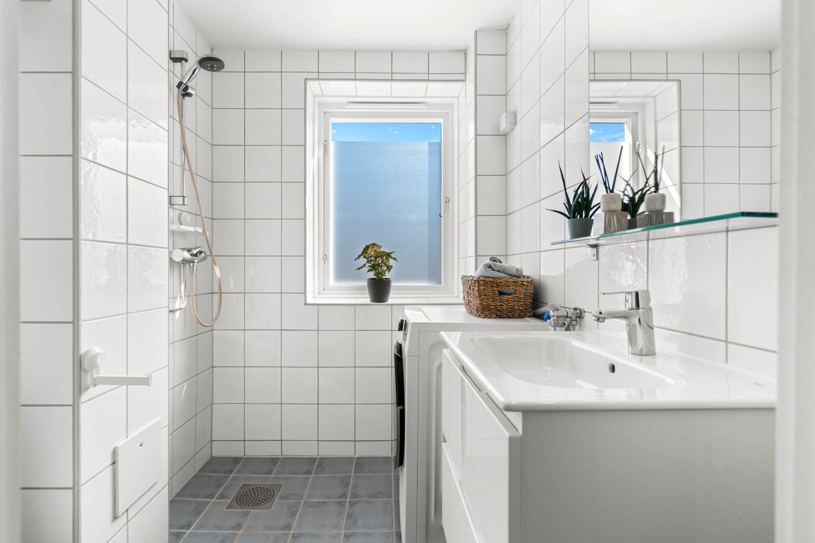 Badet er flislagt og har varmekabler i gulvet, dusjhjørne, veggmontert servant med lagring, samt opplegg for vaskemaskin Galleribilde