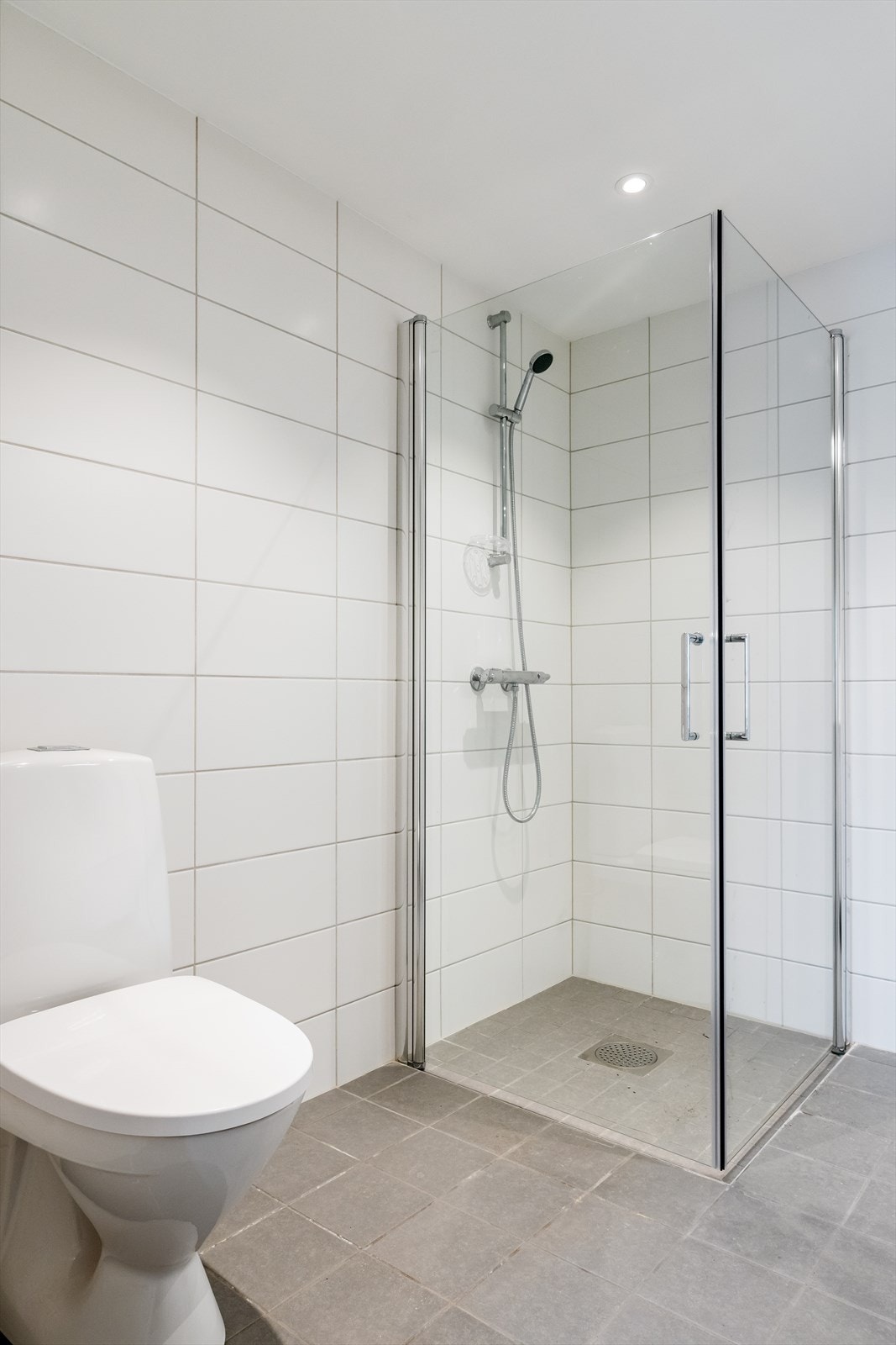 Moderne og stilrent bad med dusjhjørne. gulvmontert toalett og elegante, lyse fliser. Galleribilde