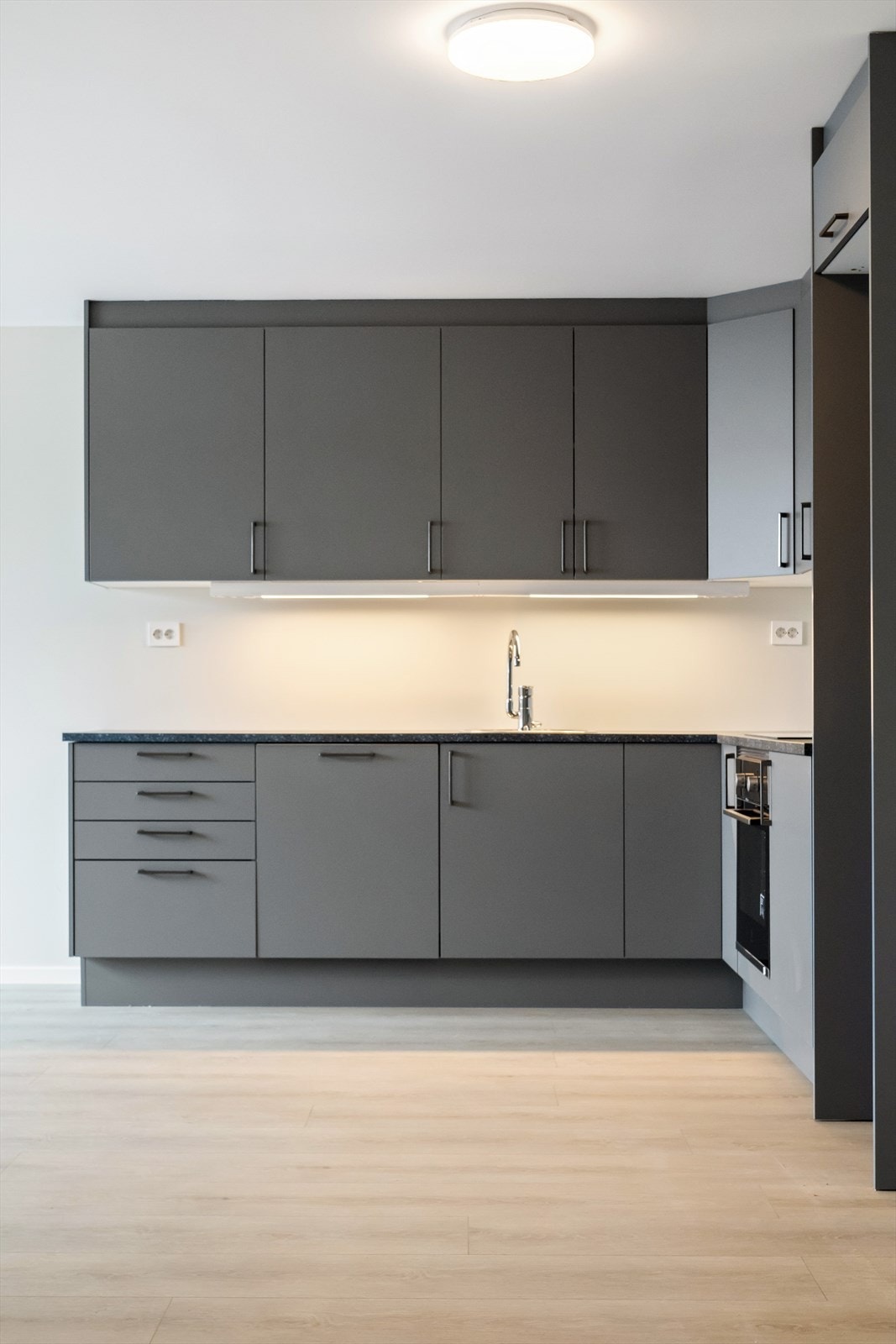 Moderne kjøkken med elegante, grå skap og innebygde hvitevarer. Lys, åpen planløsning. Galleribilde