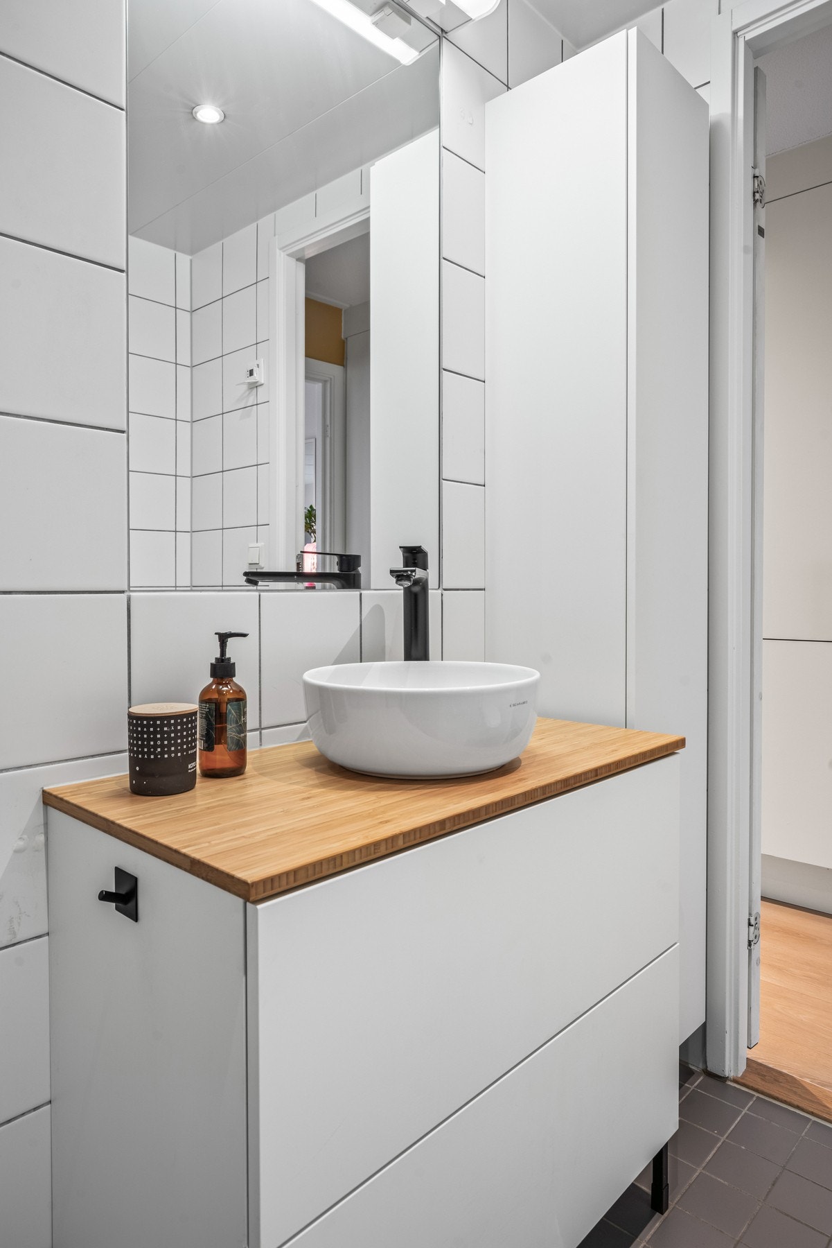 Badet er innredet med hvit baderomsinnredning med benkeplate av tre og to skuffeseksjoner. Frittstående servant over benkeplaten og speil med ekstra belysning. Galleribilde