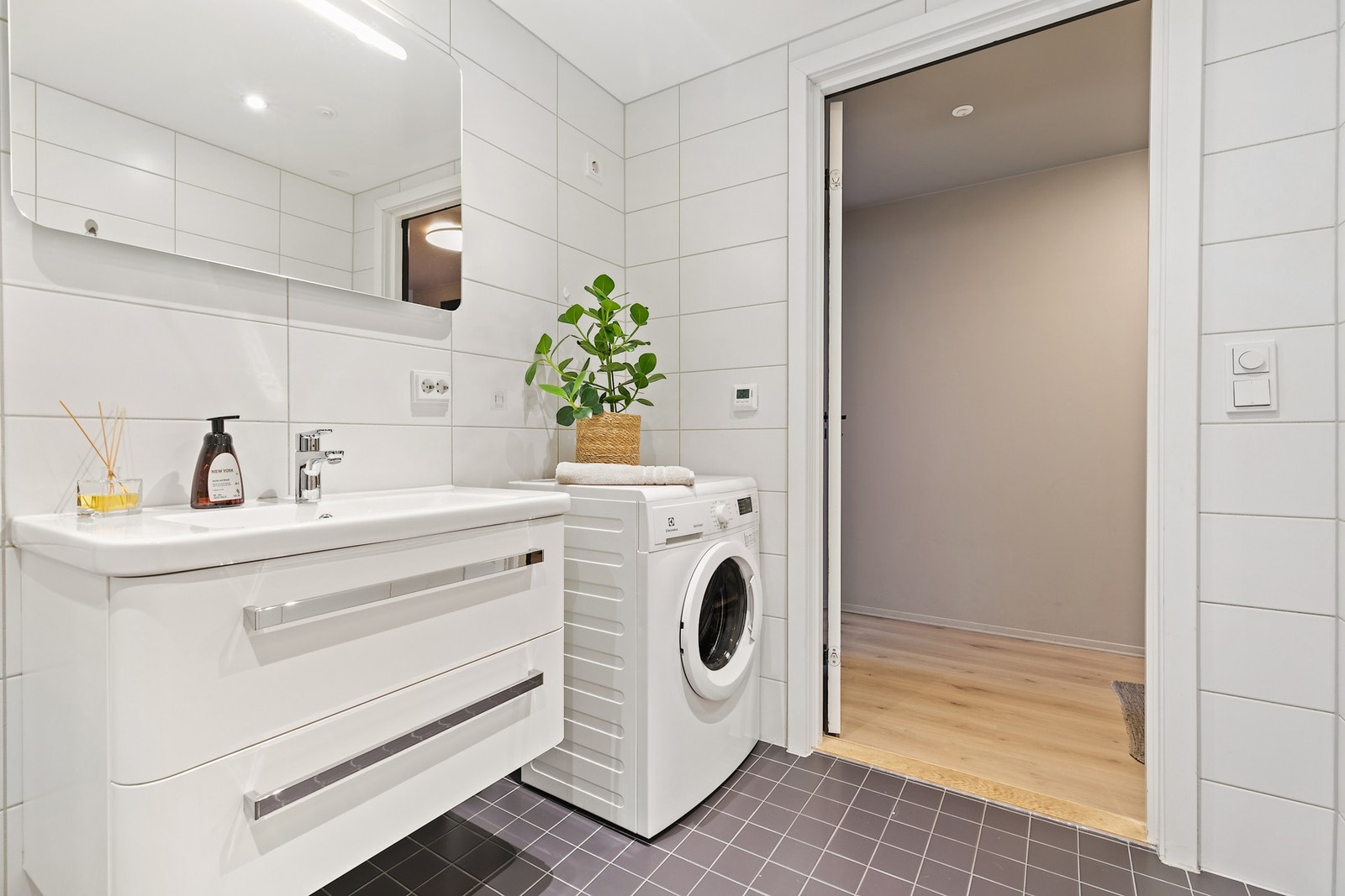 Badet har innredning med heldekkende servant med skuffeseksjon, veggmontert toalett og et dusjhjørne med glassdører. Galleribilde