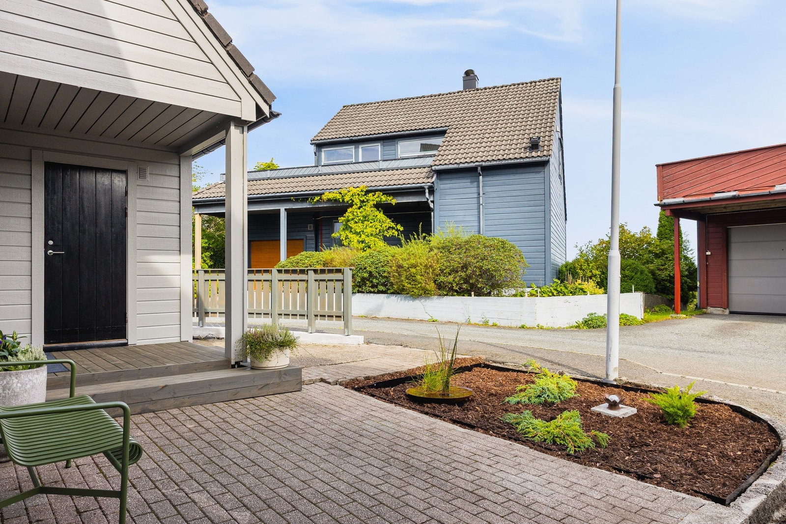 Inngangspartiet er pent opparbeidet med terrasse, belegningsstein og beplantning i et bed. Galleribilde