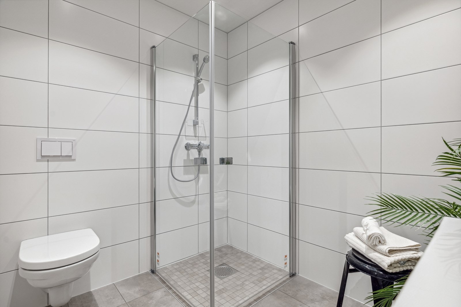 Delikat flislagt bad med vegghengt wc og dusj i nedsenket nisje med innfellbare glassdører Galleribilde