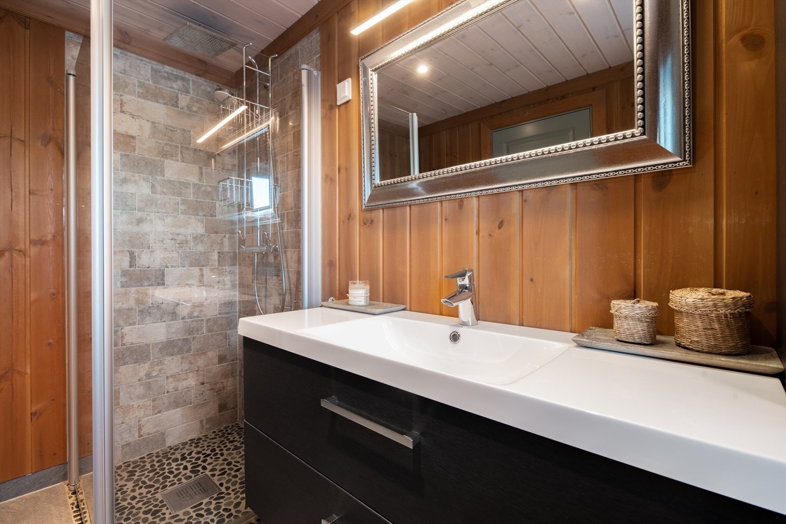 Badet er innredet med vegghengt toalett, dusjhjørne og servantinnredning med skuffer. Det er elektrisk vifte på vegg. Galleribilde