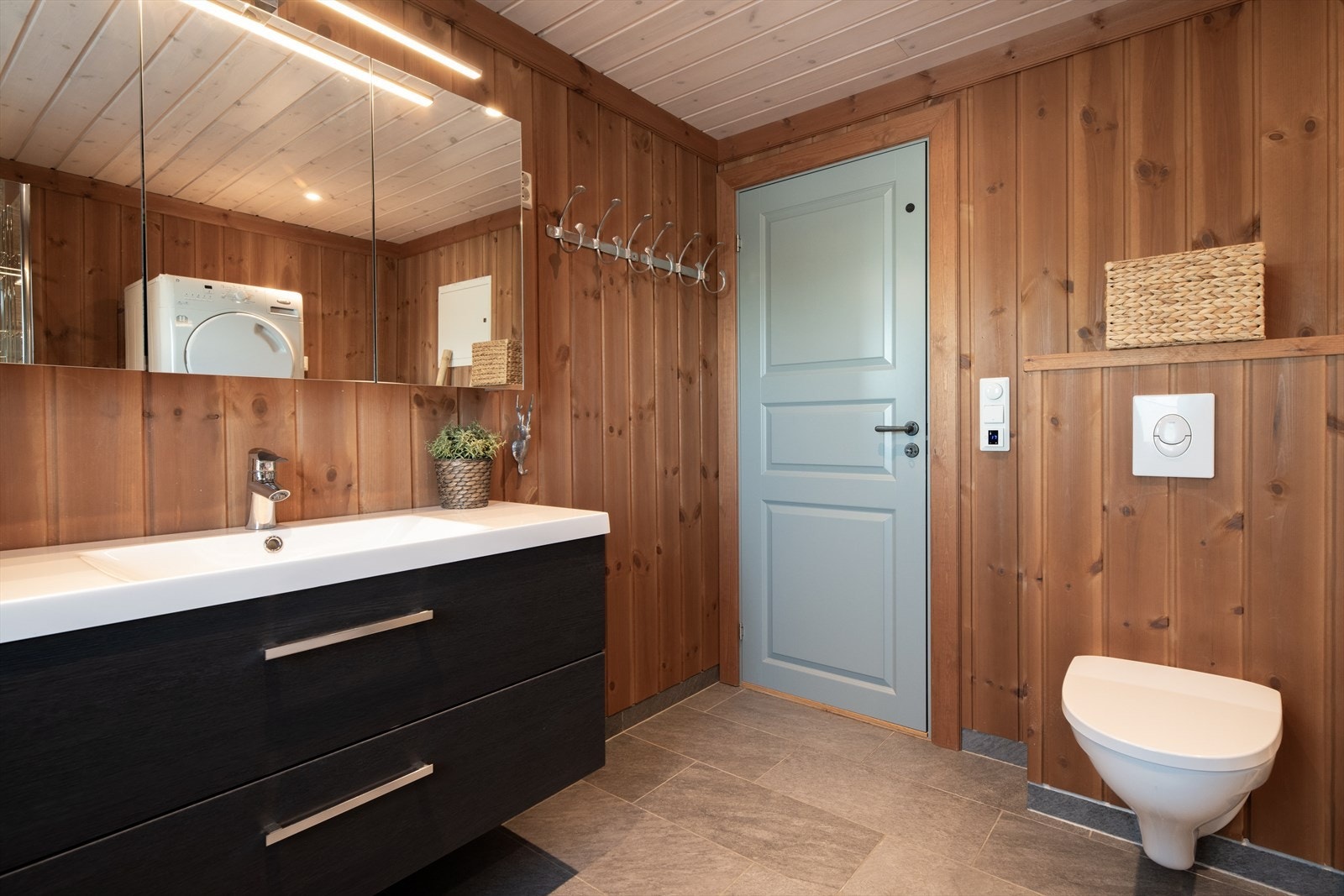 Badet har skifer på gulv med gulvvarme, panel på vegg med flis i dusjsone og panel i tak med spotter. Elektrisk vifte på vegg. Galleribilde