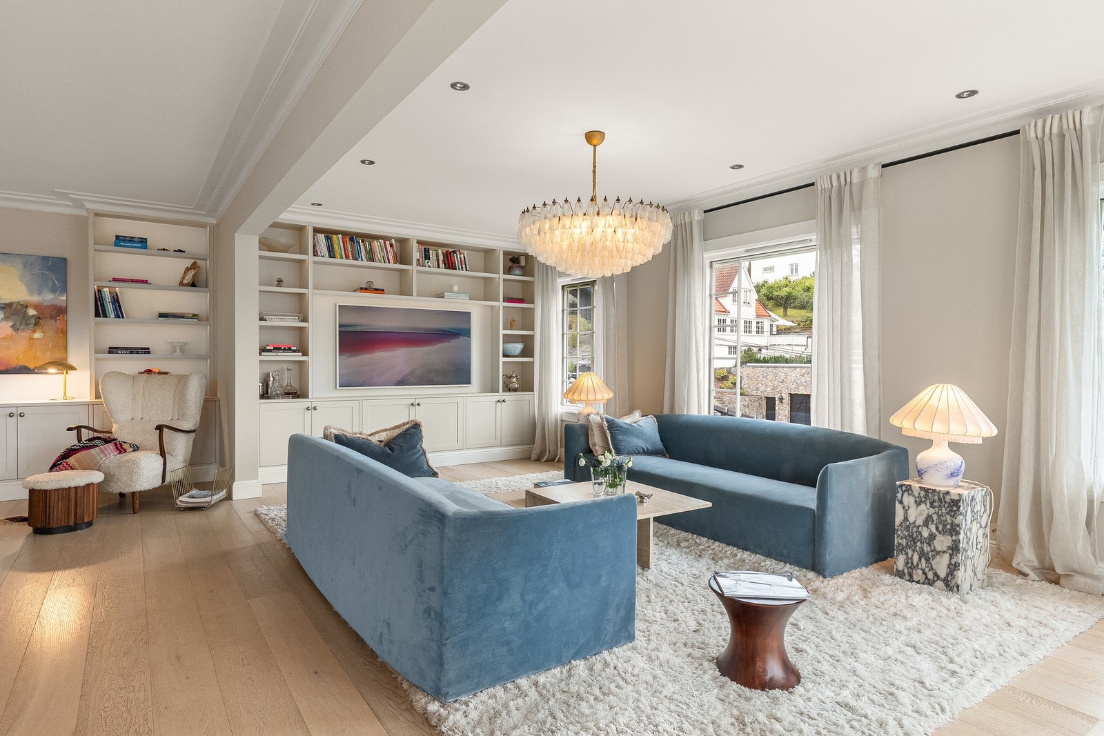 Stuen har møbelsnekret bokreol, skap og hyller med integrert belysning fra 2024 levert av Brubakken Home. Det er vegghengte minimalistiske souround høyttalere installert i stuen Galleribilde