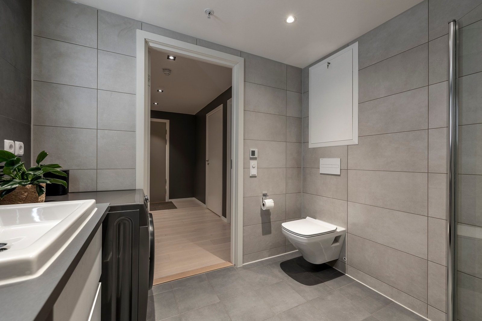 Innredningen består av servant på benk, moderne skuffeseksjon, speil med integrert belysning, vegghengt toalett og dusjhjørne med innfellbare glassdører. Galleribilde