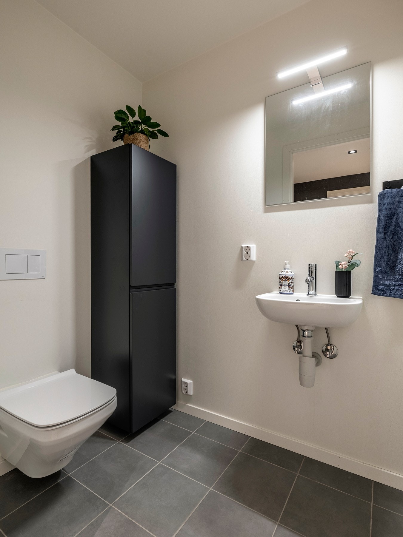 Det separate toalettrommet har samme gjennomførte stil, med grå gulvfliser, malte vegger, vegghengt toalett, speil og en moderne servant og skap ved siden av toalett. Galleribilde