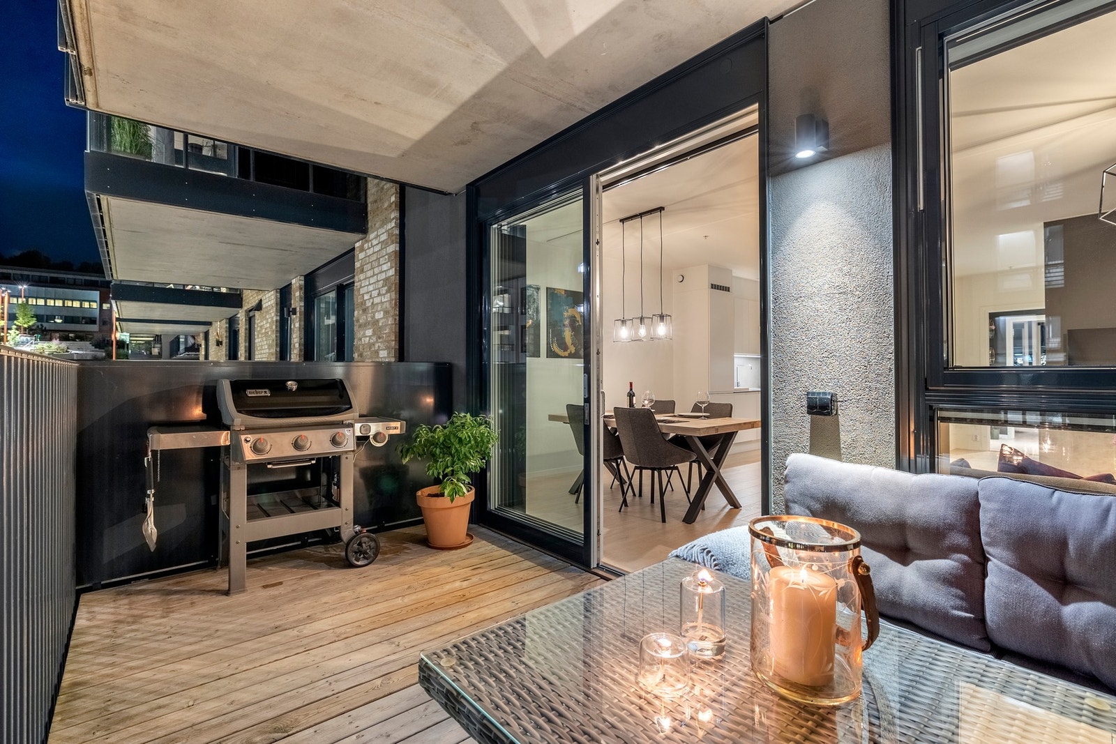 Balkongen har terrassebord på gulv, er overbygg og har rekkverk med sorte stålspiler - et moderne og stilrent uterom. Galleribilde