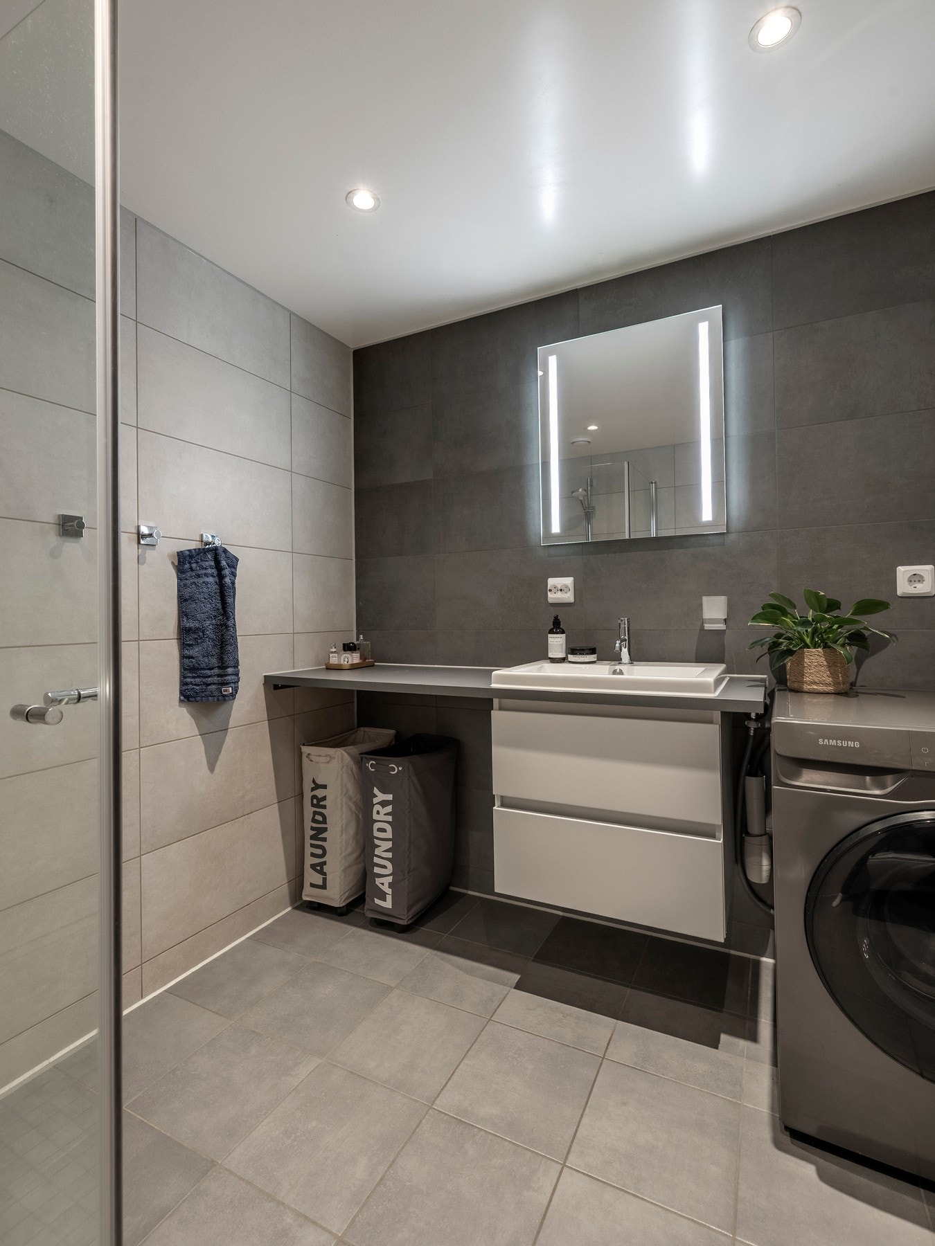 Badet er delikat innredet med grå gulvfliser, lysegrå veggfliser og en kontrastvegg i mørk grå Galleribilde