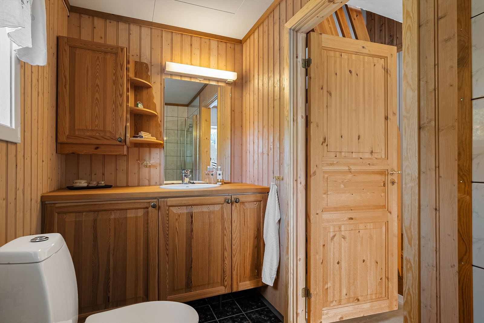 Badet er lyst og funksjonelt, med fliser på gulv og kombinasjon av flis og panel på vegger. Galleribilde