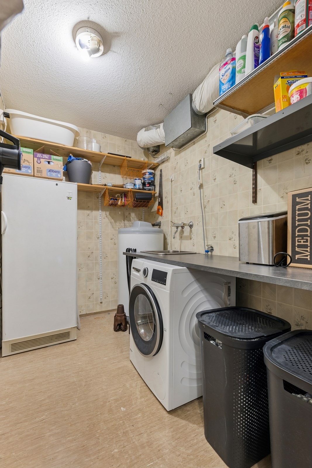 Videre finner man et vaskerom innredet med vinylbelegg på gulv og tapet på vegg. Vaskerommet er ellers utstyrt med utslagsvask, benkeplass og opplegg for vaskemaskin. I tillegg har man godt med hyller som gir god lagringsplass. Galleribilde