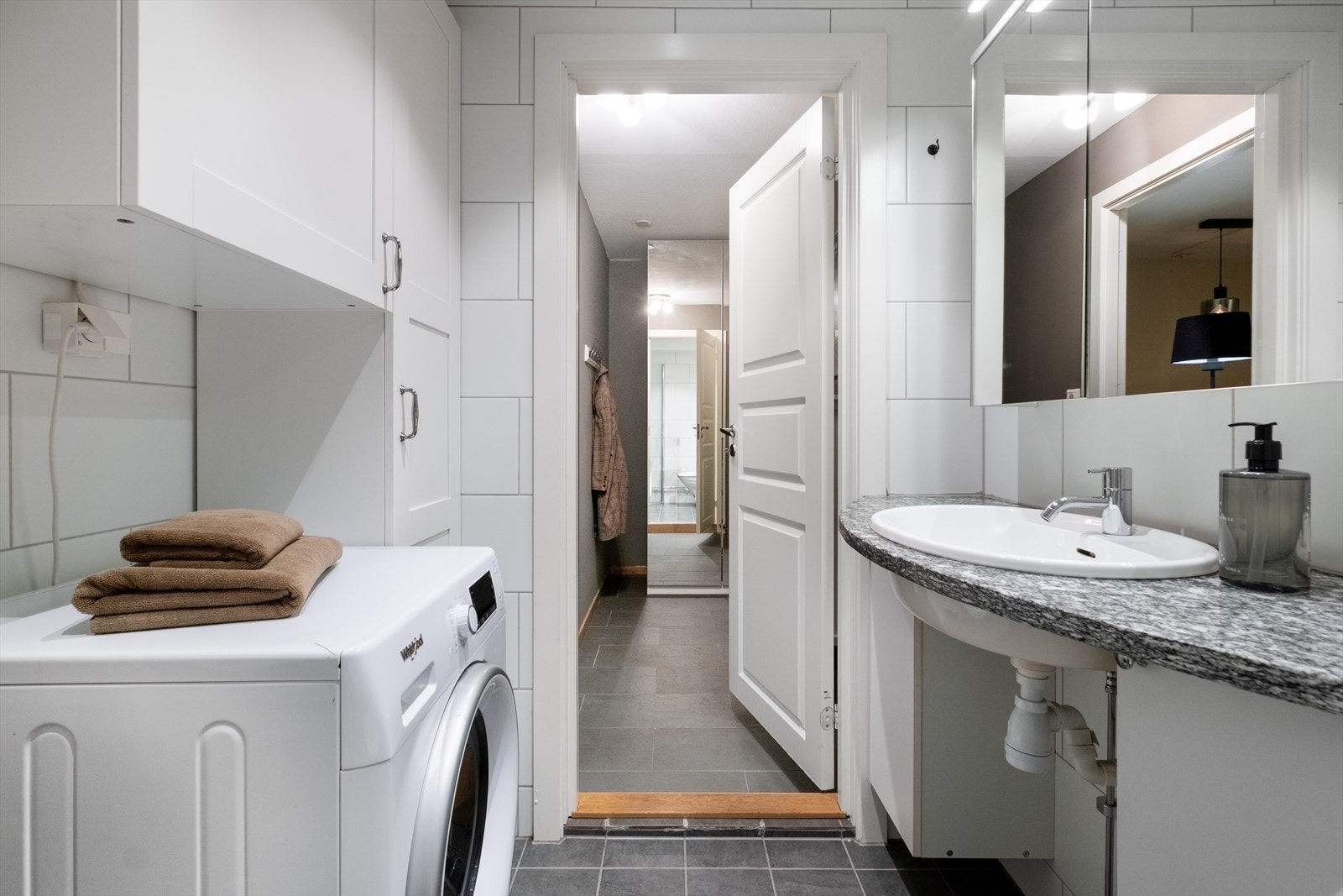 Innredningen består av nedfelt servant med tilhørende skap, veggmontert toalett og dusjhjørne med glassvegger - det er også opplegg for vaskemaskin, og et praktisk høyskap gir godt med oppbevaringsplass Galleribilde