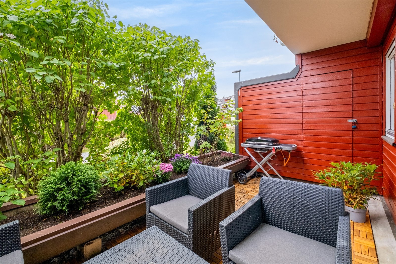 Terrassen har tredekke, levegger mot inngangspartiet, utvendig bod som skjermer mot naboen, og blomsterkasser med busker i front som gir både grønn utsikt og god skjerming Galleribilde